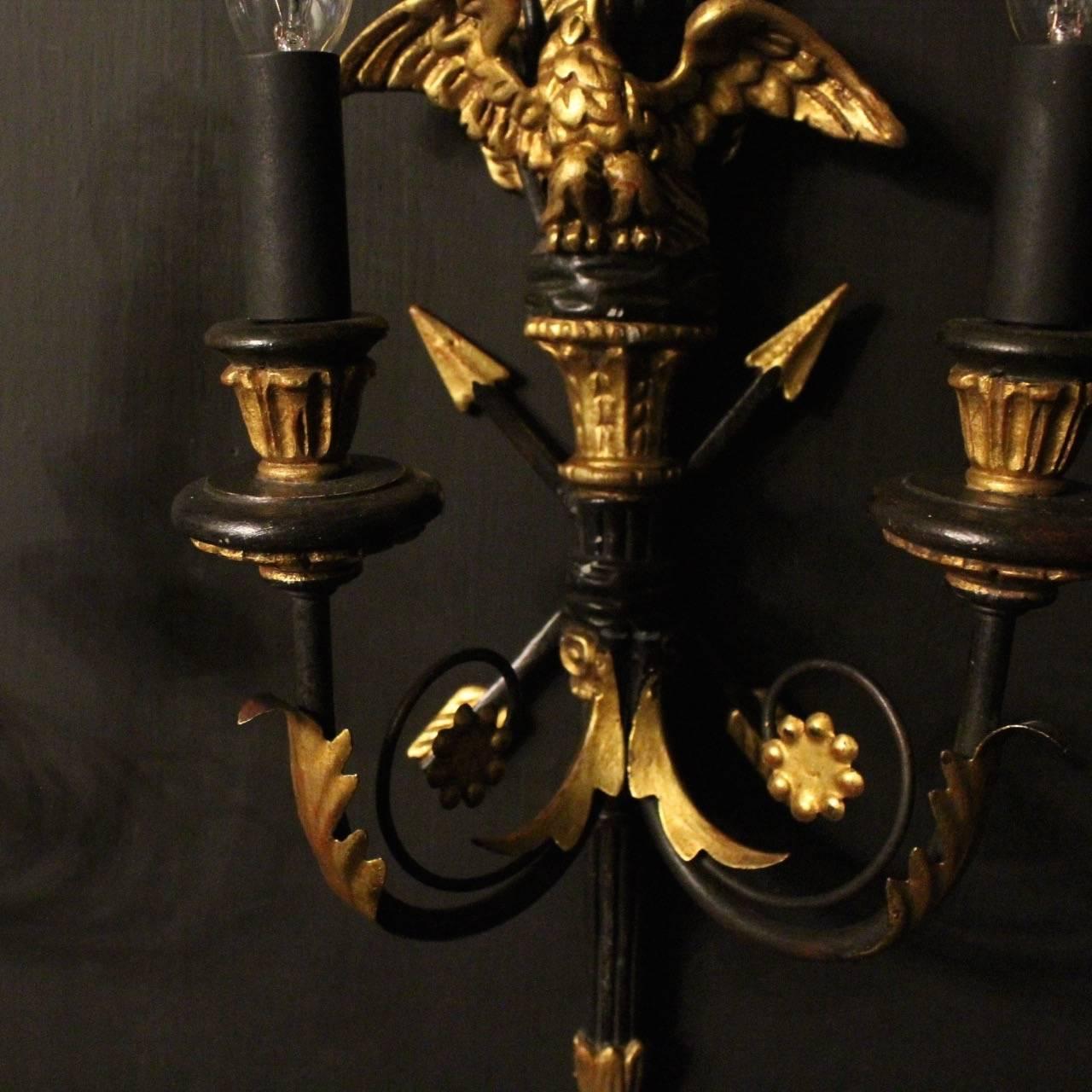 A decorative set of four Italian ebonized, giltwood and toleware wall lights, the iron acanthus leaf scrolling arms with wooden circular bobeche drip pans and reeded candle sconces, issuing from an ebonized elongated reeded tapering backplate with