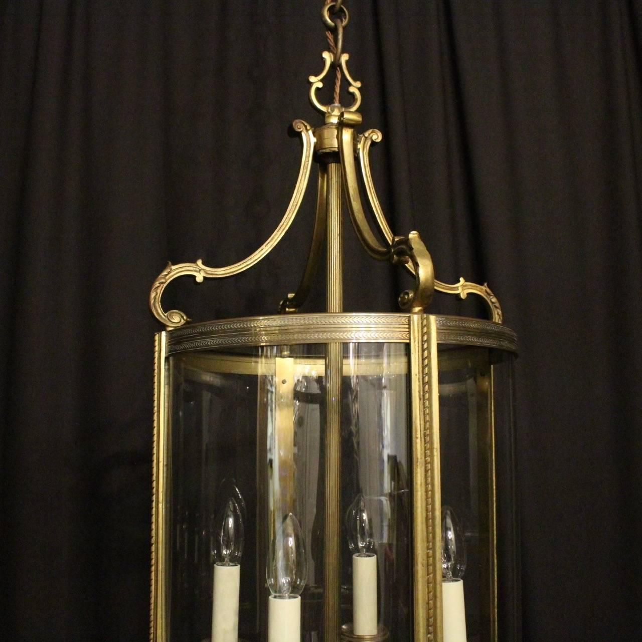 Large French gilded cast bronze four light antique hall lantern, the four ornate scrolling light fittings with circular bobeche drip pans, surrounded by four sectional convex glass panels and held within an ornately cast scrolling framework with