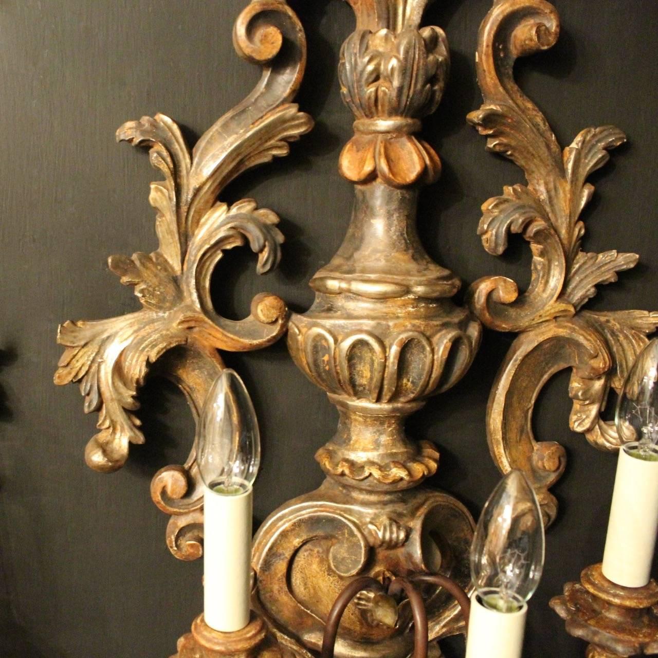 A decorative Italian carved polychrome giltwood and toleware triple arm wall lights, the foliated toleware leaf scrolling arms with wooden bulbous candle sconces, issuing from an ornate pierced Acanthus leaf silvered wooden backplate with reeded