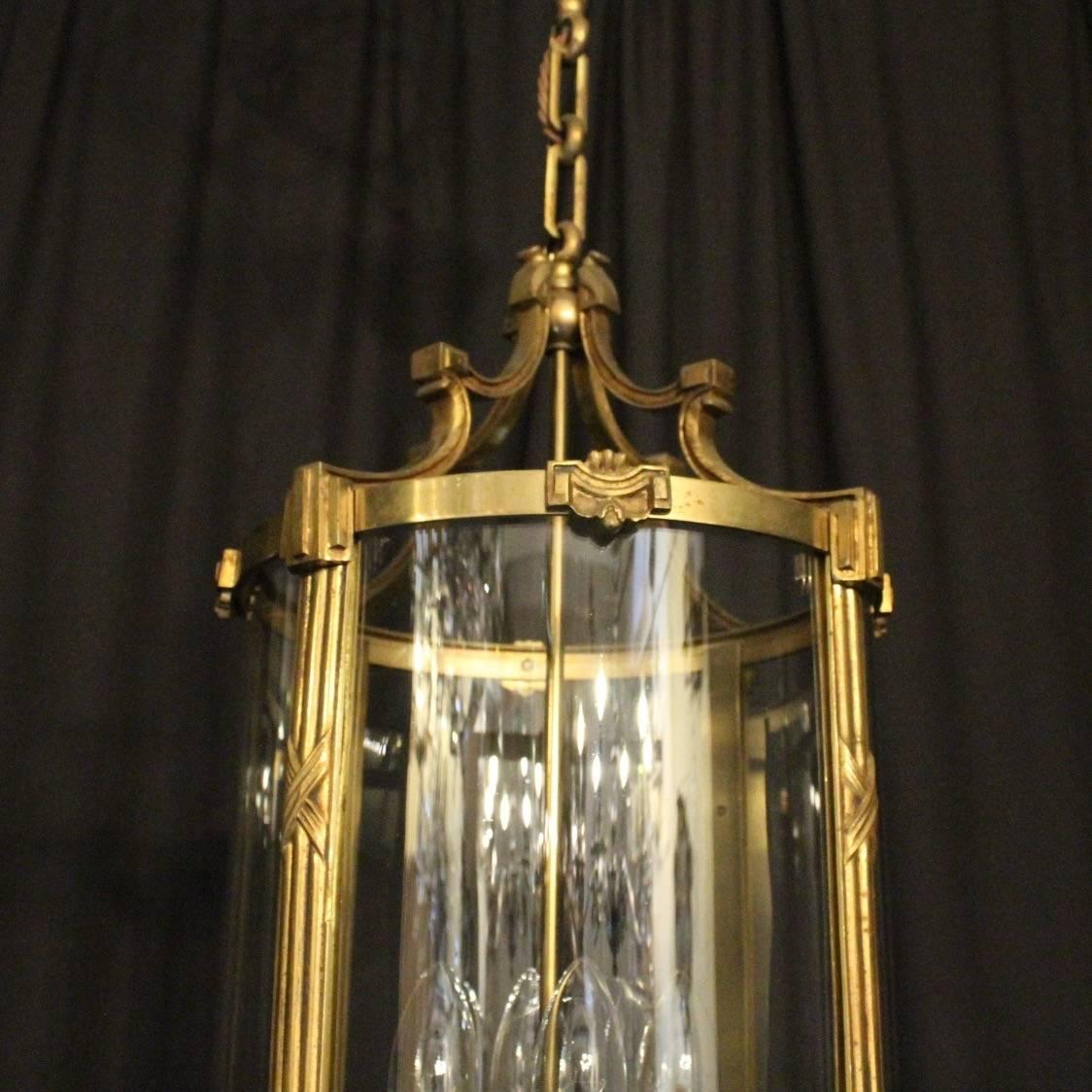 A French gilded cast bronze four-light antique hall lantern, the reeded bulbous candle sconces, surrounded by four sectional circular convex glass panels and held within an ornately cast heavy gauge scrolling framework with side reeded panels,