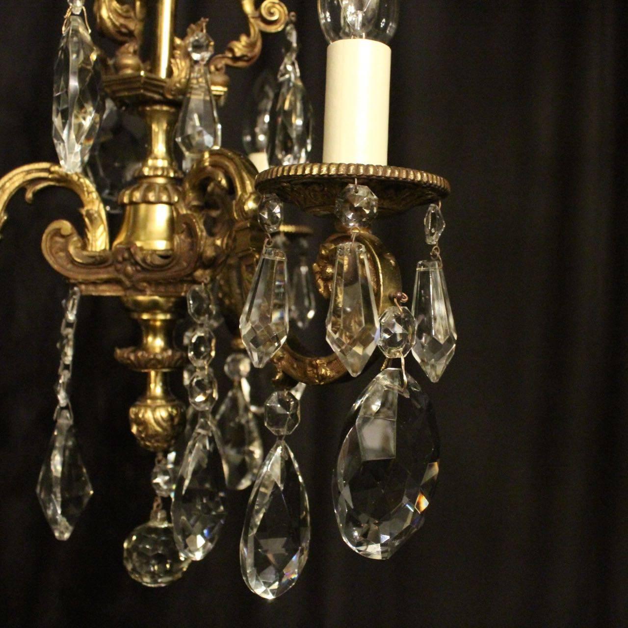 A French gilded cast brass and crystal triple light antique chandelier, the three leaf detailed square gauge scrolling arms with circular bobeches drip pans, issuing from a central cage with ornate winged lady embellishments, decorated overall with