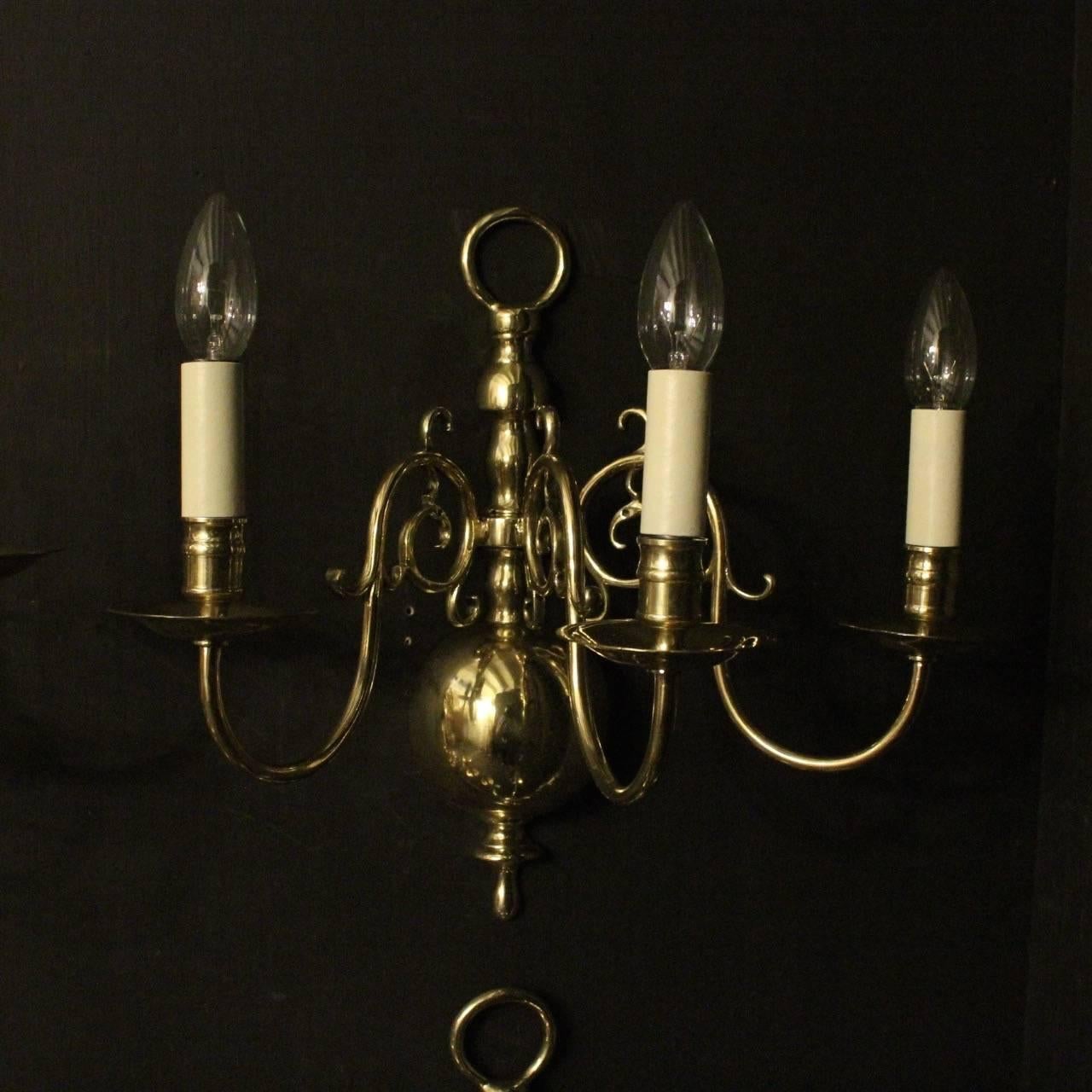 An English set of four repolished triple arm cast brass antique wall sconces, the scrolling arms with circular cast bobeche drip pans and bulbous candle sconces, issuing from a large elongated baluster knopped backplate, sympathetically repolished,