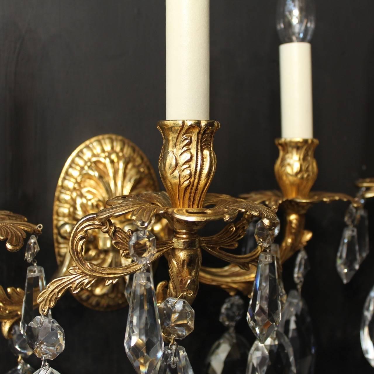 A Large Italian pair of gilded cast bronze and crystal triple arm wall lights, the leaf scrolling arms with pierced leaf bobeches drip pans and bulbous candle sconces, issuing from an Elliptical leaf backplate decorated with large quality crystal