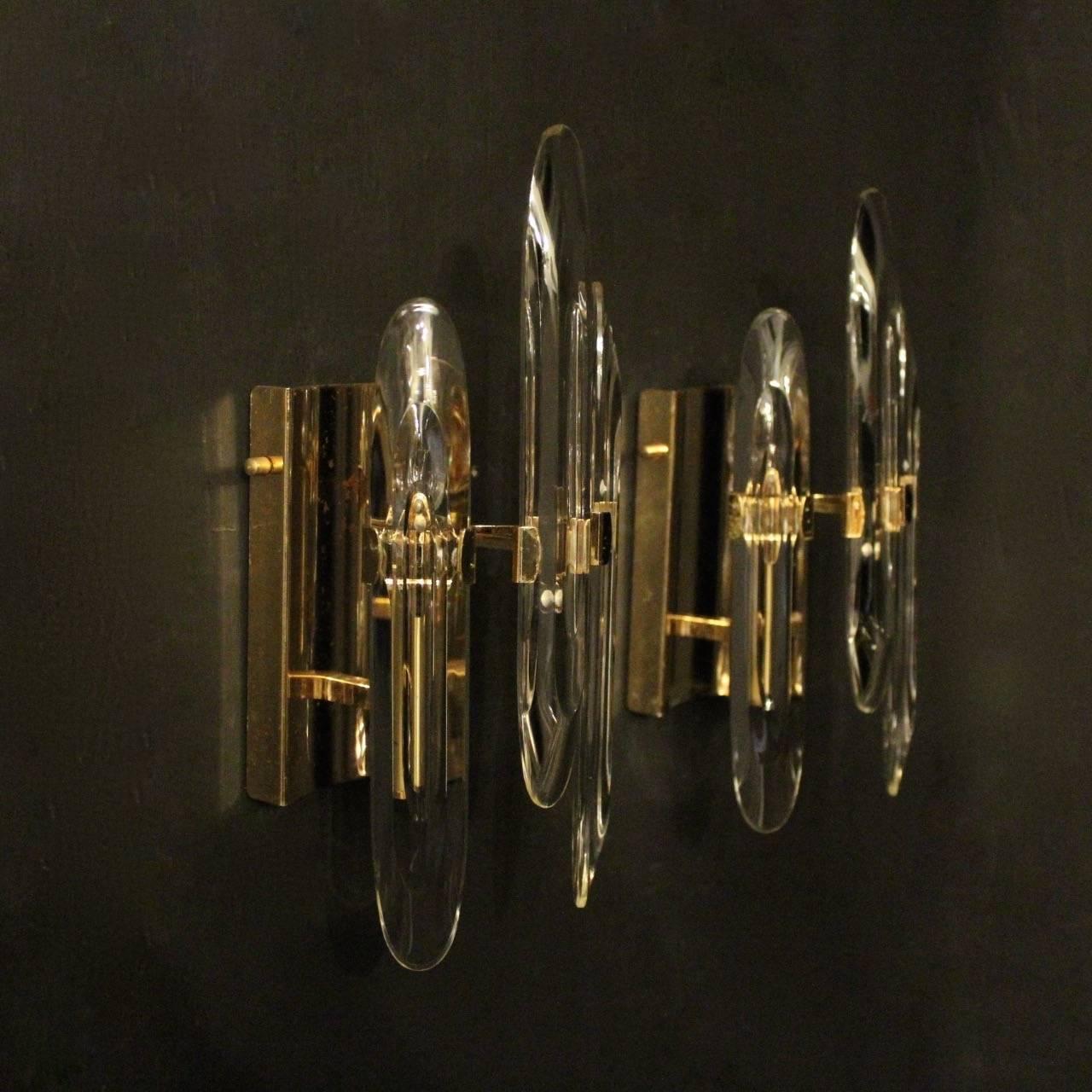An Italian pair of gold plated brass single arm Gaetano Sciolari lights, the three elongated bevelled crystal rods set in front of a single light fitting, issuing from a rectangular backplate, nice original patination and good size, designed by