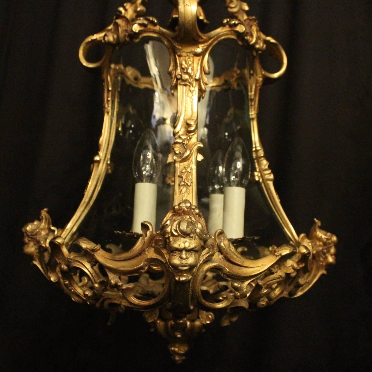 An elaborate pair of Italian gilded cast bronze four-light cherub lanterns, the four scrolling light fittings surrounded by four sectional concave glass panels and held within an ornately cast leaf pierced scrolling framework with acanthus leaf