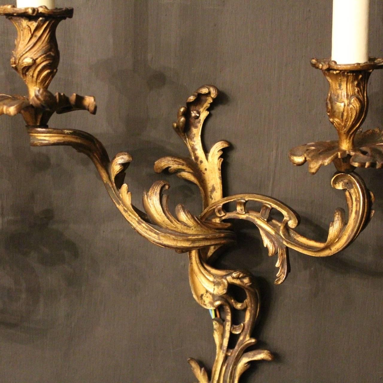 A French pair of gilded bronze twin arm antique wall sconces, the acanthus leaf scrolling arms with leaf bobeche drip pans and bulbous candle sconces, issuing from an ornate leaf pierced backplate, good original gilded patination and nice