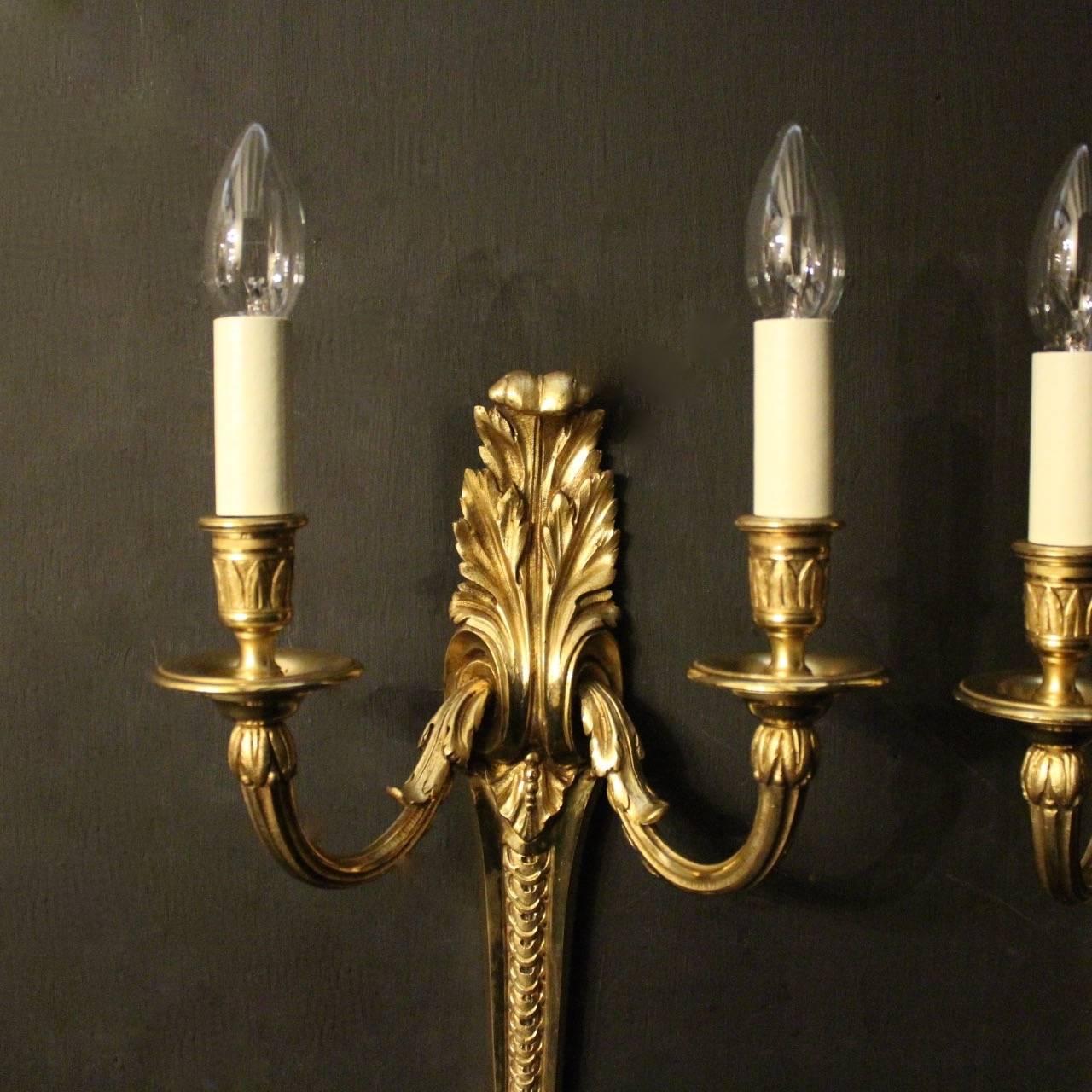 A large French pair of gilded bronze twin arm antique wall lights, the reeded scrolling arms with circular bobeche drip pans and leaf candle sconces, issuing from an elongated tapering imbricated ornate leaf backplate with acanthus leaf finial,