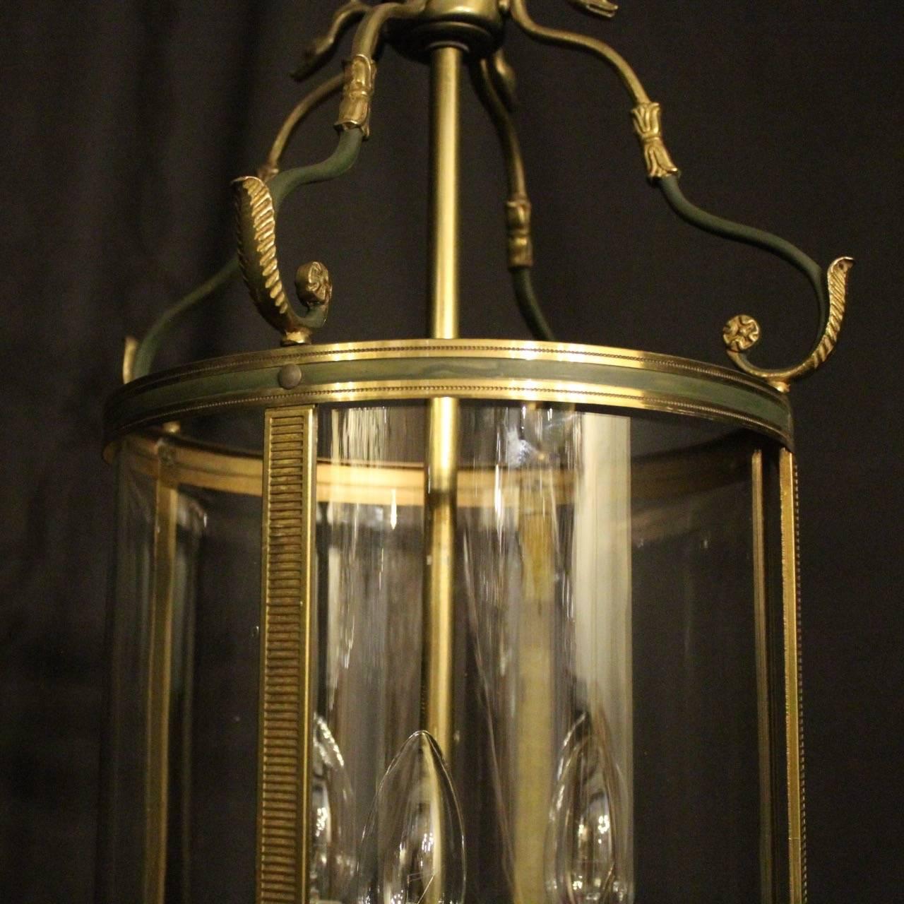A French Empire gilded cast brass triple light antique hall lantern, the three light fittings with circular reeded bobeche drip pans, surrounded by a single circular convex glass panel, held within a decorative cast scrolling framework with green