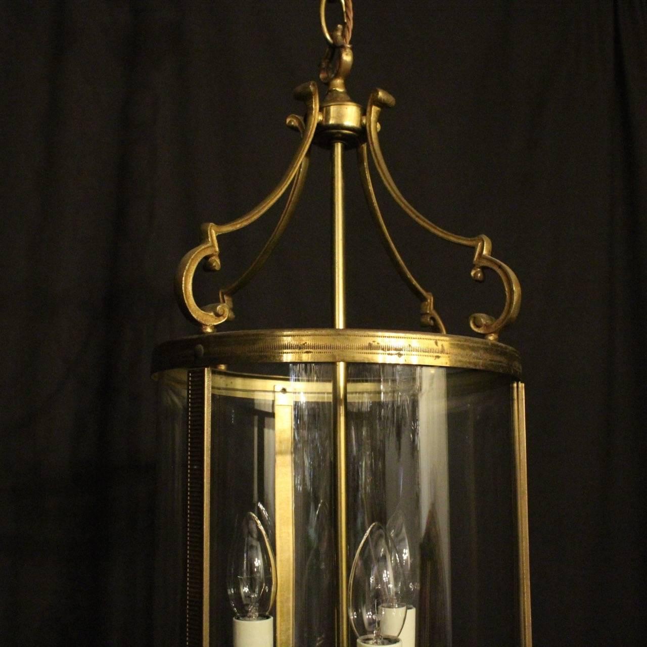 A French pair of gilded cast brass triple light antique hall lanterns, the three-light fittings with circular bobeche drip pans, surrounded by a single circular convex glass panel, held within a decorative cast scrolling framework with reeded