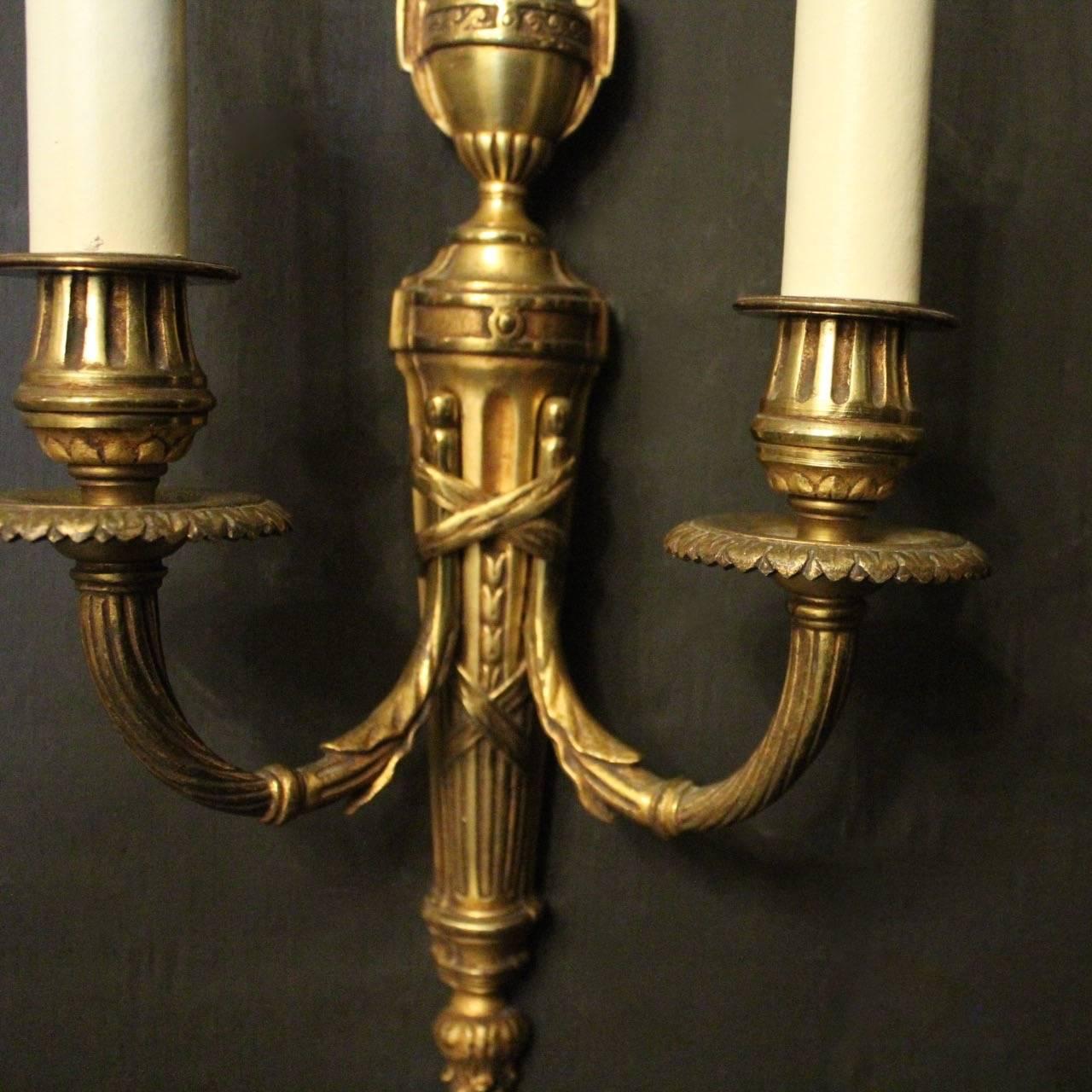 A French pair of gilded bronze twin-branch antique wall lights, the barley twisted reeded scrolling arms with circular leaf bobeche drip pans and reeded bulbous candle sconces, issuing from a tapering reeded back plate with flame urn finial, good
