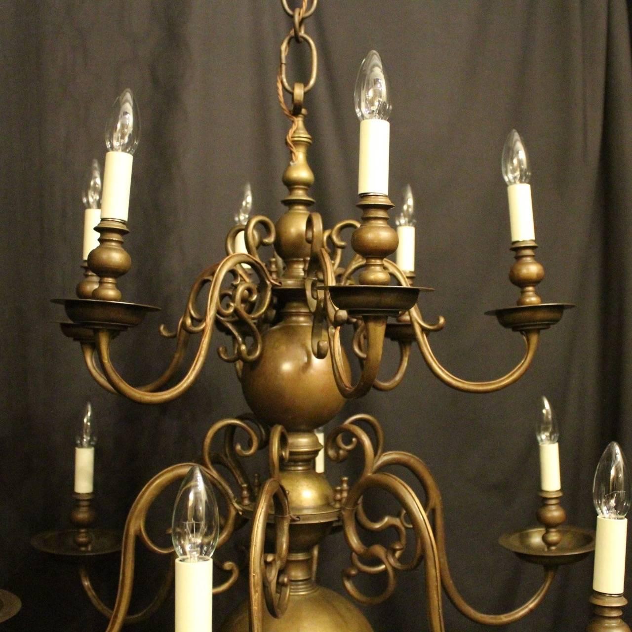 A large Flemish bronze twelve-light double tiered antique candle chandelier, the removable scrolling arms with large stepped circular bobeche drip pans and bulbous candle sconces, issuing from a knopped central column with pierced ring finial with