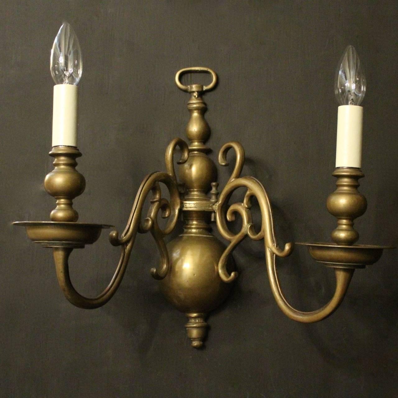 A Flemish set of four bronze twin-arm antique wall sconces, the scrolling arms with circular cast bobeche drip pans and bulbous candle sconces, issuing from a large elongated baluster knopped backplate, nice original faded oxidised patination and