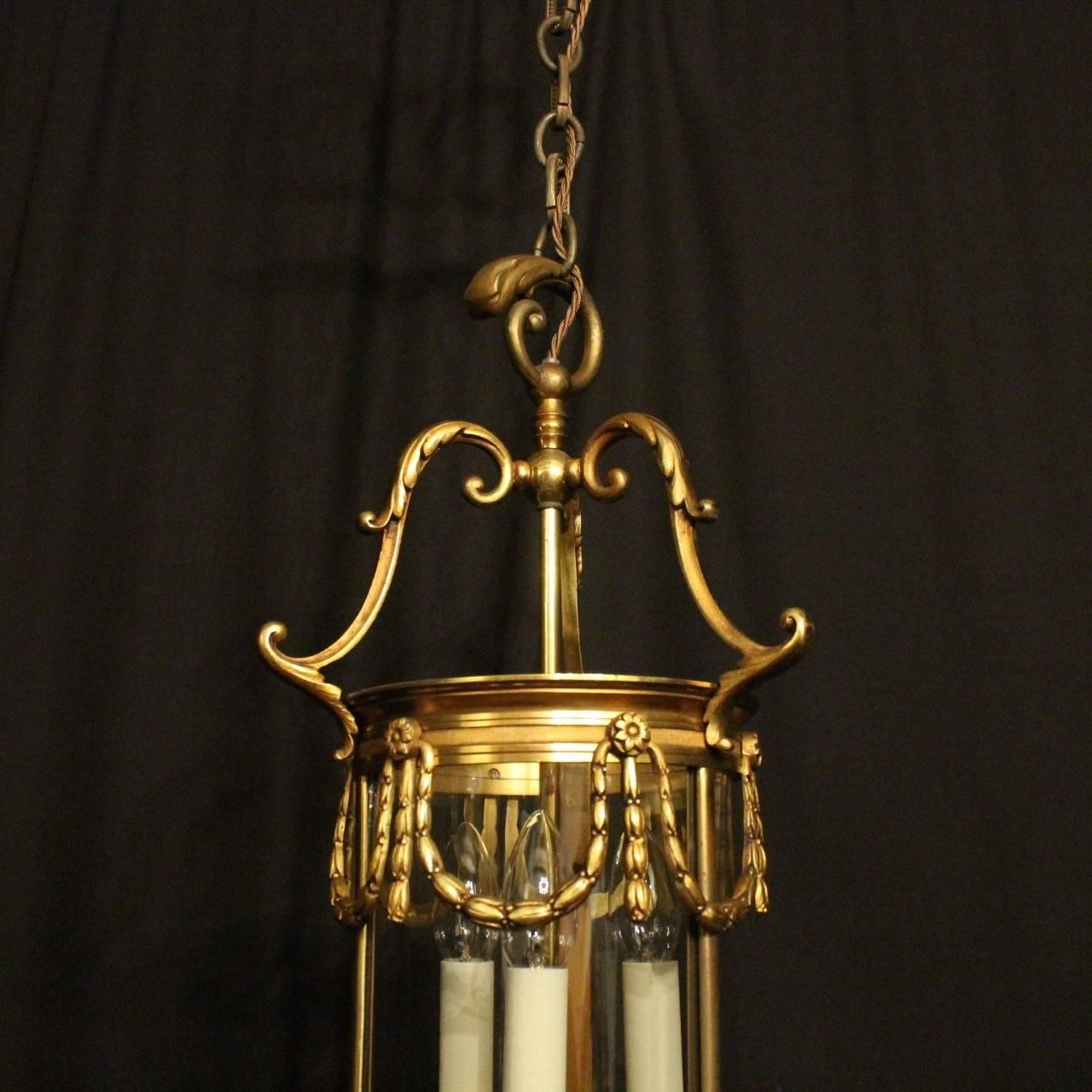 A French gilded bronze triple light convex antique hall lantern, the three light fittings surrounded by three sectional convex glass panels and held within an ornate acanthus leaf scrolling framework with reeded banding, swaged laurel leaf