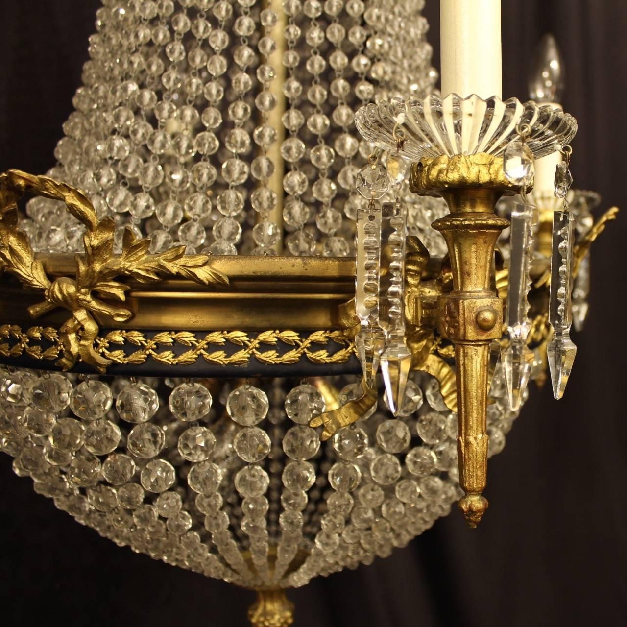 A French gilded cast bronze and crystal ten-light waterfall antique chandelier, the four torchere arms with reeded glass bobeche drip pans, with six internal light fittings, issuing from an ornately cast black leaf clad enamelled band with laurel