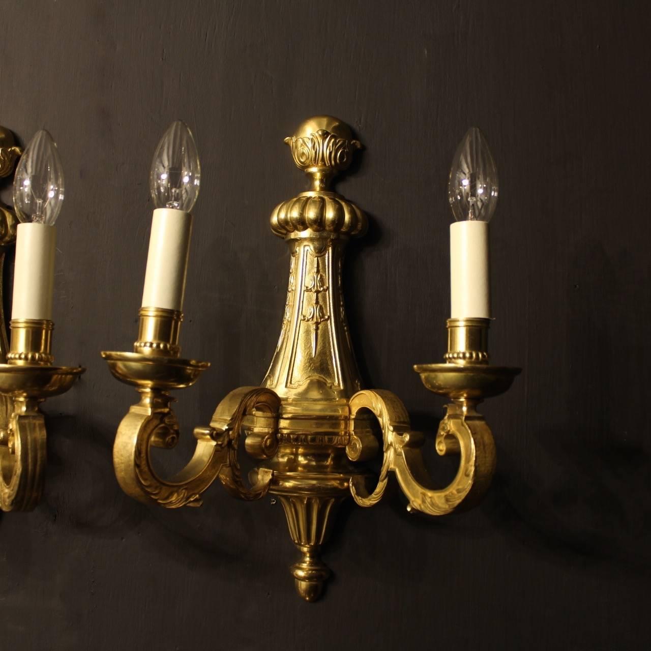 A set of six French bronze twin branch antique wall lights in the Louis XIV taste, the scrolling leaf square gauge scrolling arms with circular bobeche drip pans and millgrain candle sconces issuing from a foliate moulded backplate with decorative