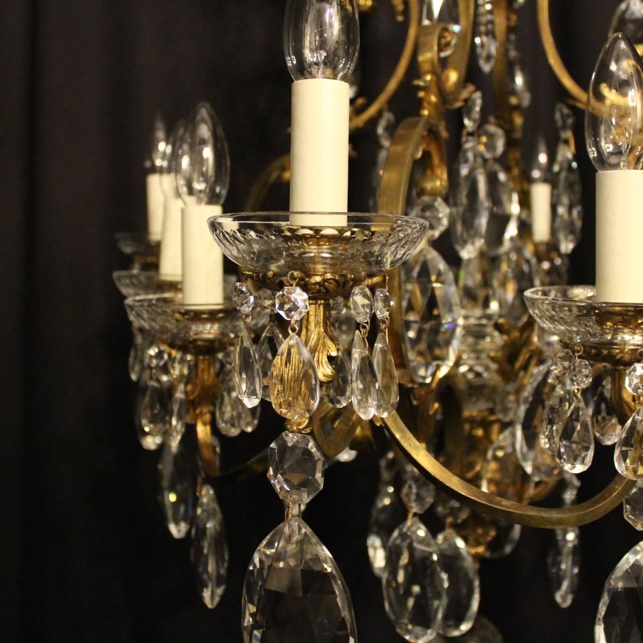 A French gilded cast bronze and crystal twelve-light birdcage form antique chandelier, the square gauge leaf scrolling arms with glass bobeche drip pans and leaf candle sconces, issuing from an foliated cage form interior with a large prismatic