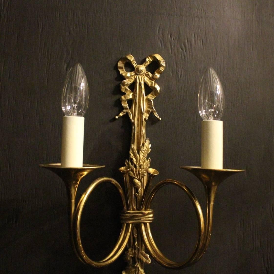 A French pair of gilded cast brass twin arm Maison Baguès wall lights, the scrolling trumpet bobeche drip pans and leaf bulbous candle sconces, issuing from a decoratively cast elongated rope and tassel pierced backplate, nicely cast and good crisp