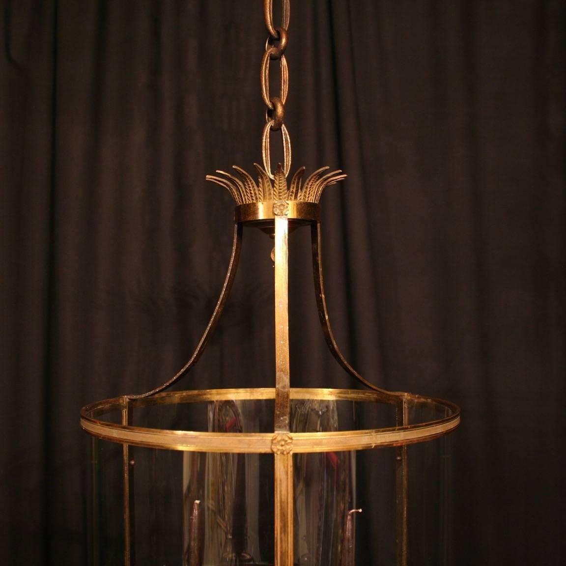 A large French gilded cast bronze triple candle sconce antique hall lantern, the three scrolling light fittings surrounded by three sectional circular convex glass panels and held within a cast scrolling framework with simple circular banding,