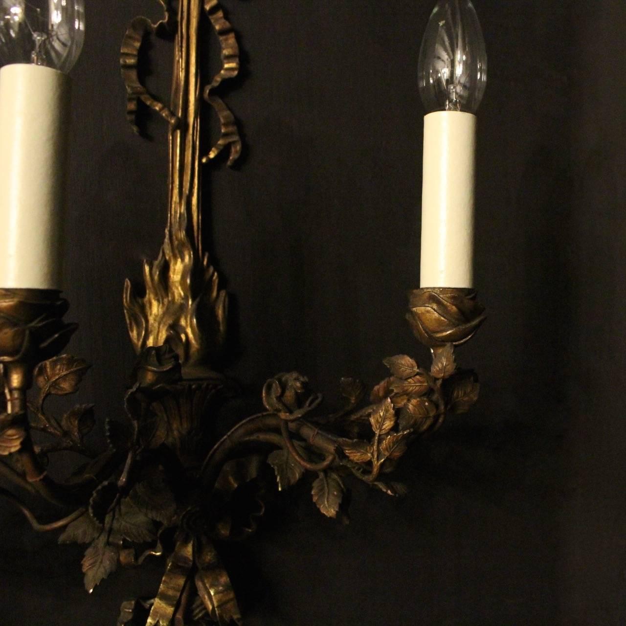 A large pair of English gilded bronze twin arm antique wall sconces, the leaf and flower scrolling arms with decorative leaf bulbous candle sconces, issuing from a decoratively cast elongated flame backplate, centring large pierced bow with a ribbon