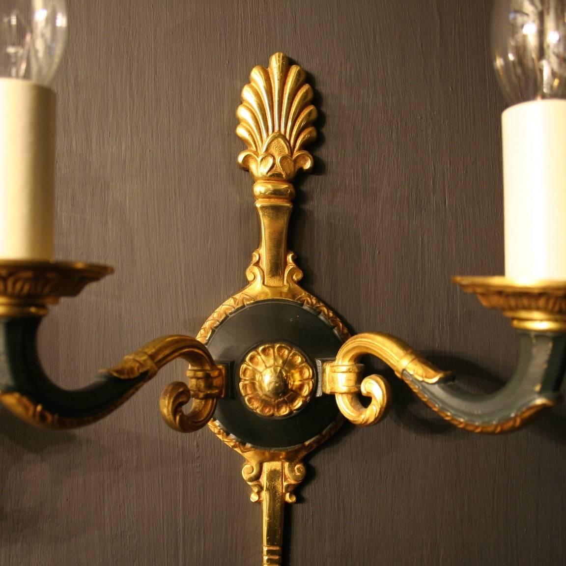 A French pair of gilded cast bronze twin arm antique wall lights, the reeded leaf scrolling arms with circular leaf bobeche drip pans, issuing from green enamelled circular backplate with decorative Anthemion finial and arrow head terminal, nice