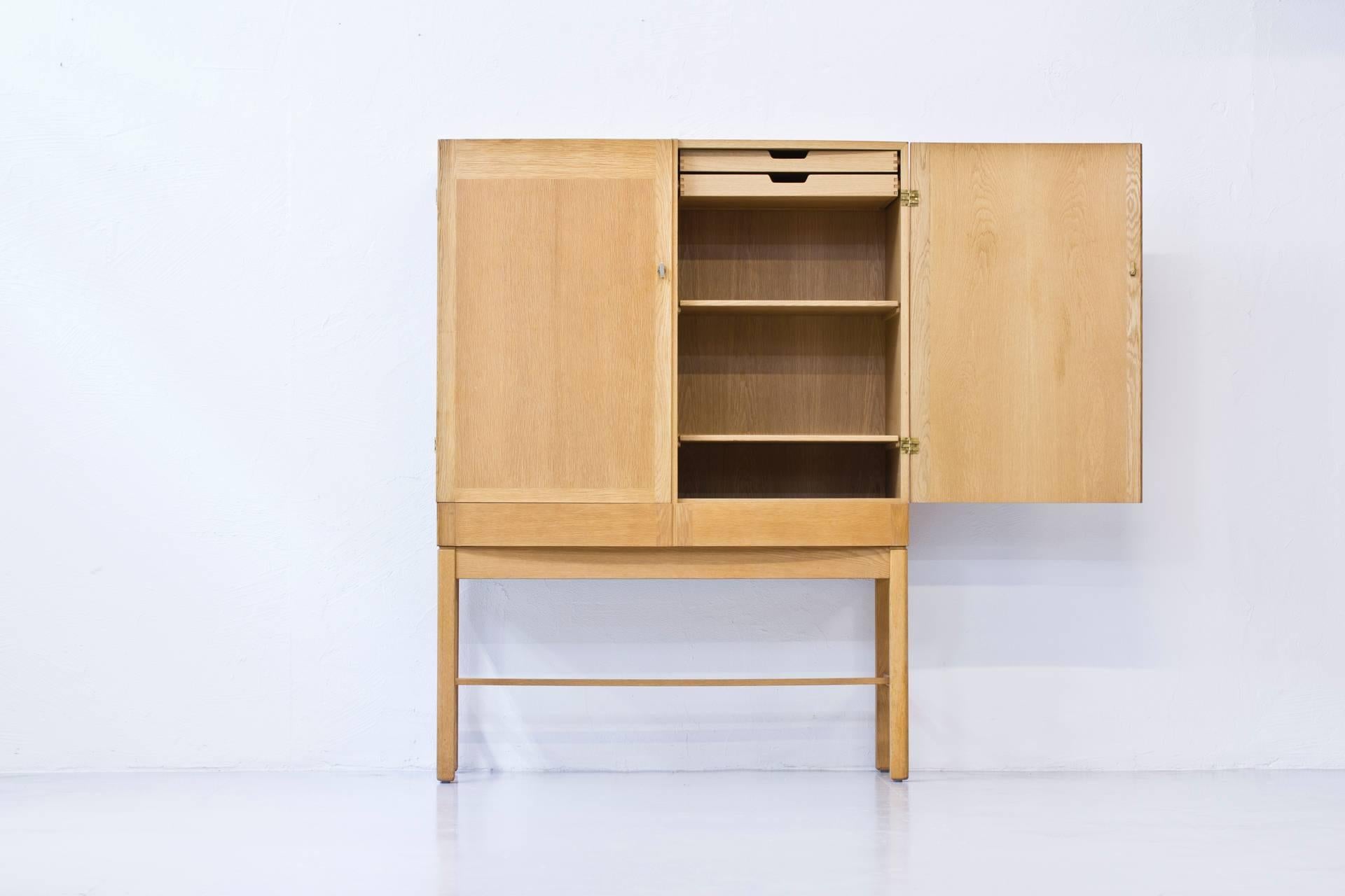 Rare oak cabinet designed by Gunnar Myrstrand in the 1960s. Produced in Sweden by Källemo. With solid brass handles. Adjustable shelves. Slightly curved front. Signed. Good vintage condition with small restoration on the top of the doors.
 