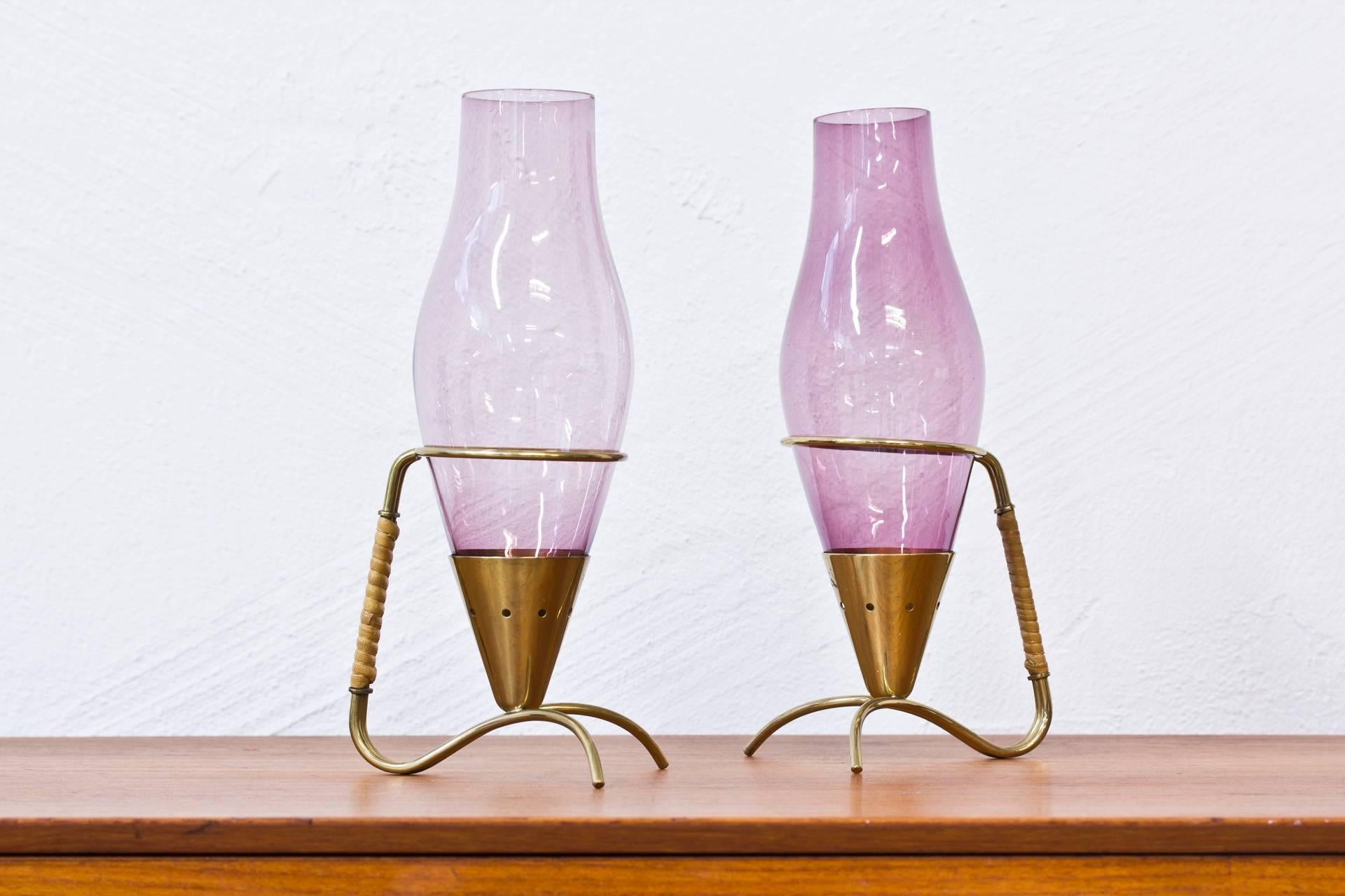 Pair of candlesticks designed by Gunnar Ander. Produced in Sweden during the 1950s by Ystad Metall. Polished brass with handblown purple glass shades and rattan handles.