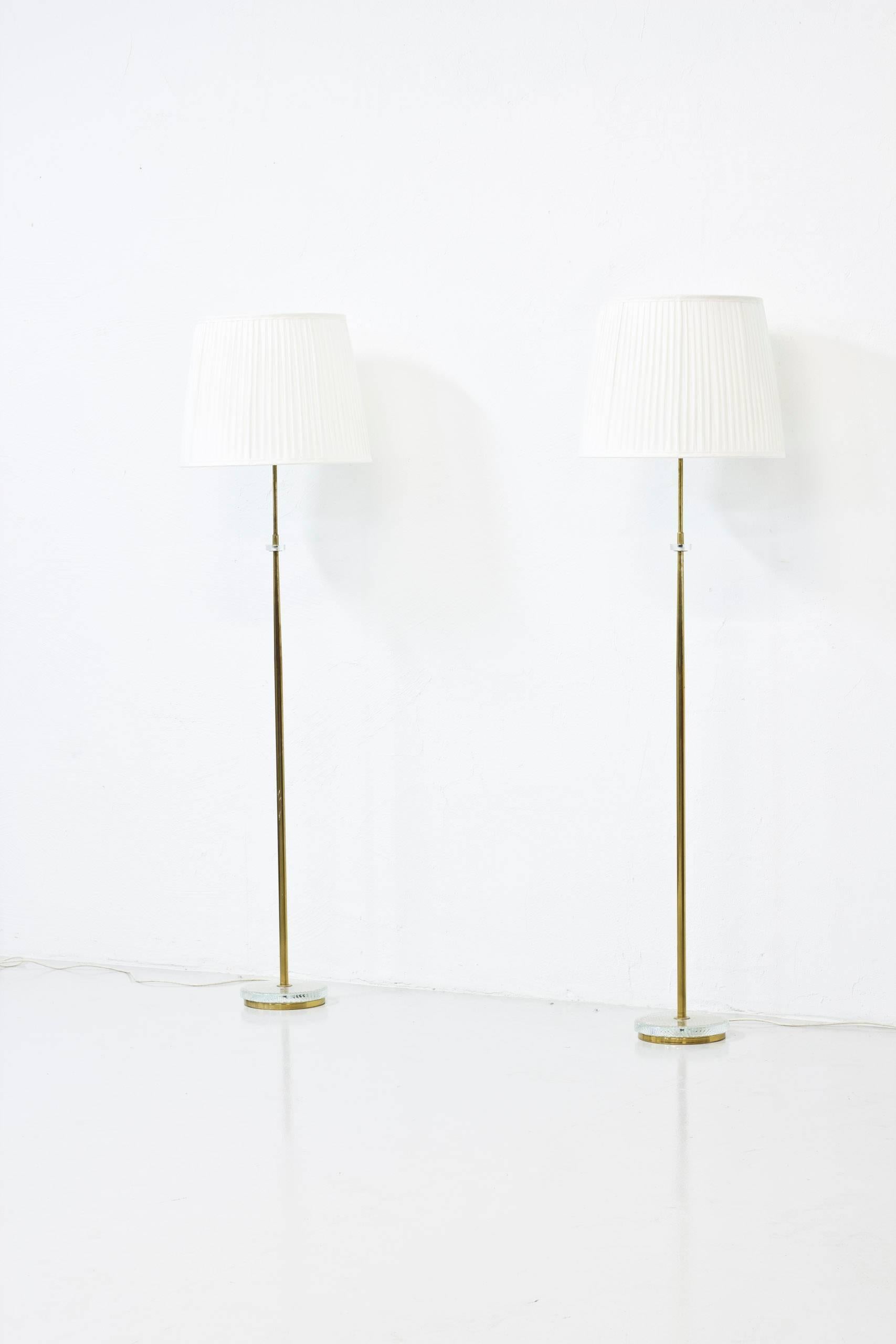 Pair of floor lamps in polished brass with clear glass details. New hand-sewn pleated silk shades. Produced in Sweden by CeBe during the 1960s. All original with light switch on the fixture in working condition. New electric cables. Excellent