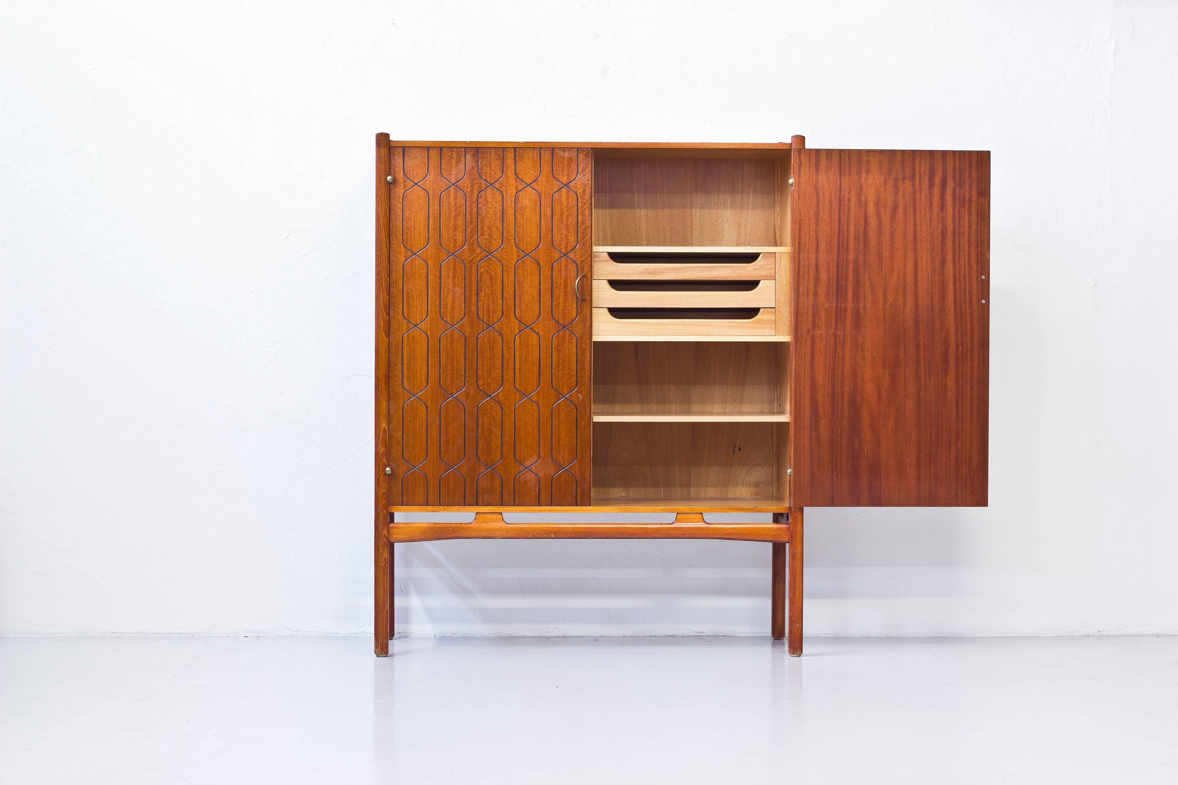 Cabinet designed by David Rosen. Produced in Sweden by Nordiska Kompaniet during the 1950s. Mahogany and beech wood with brass details. Adjustable shelves on the inside and three drawers. Very good condition with few signs of wear and light age