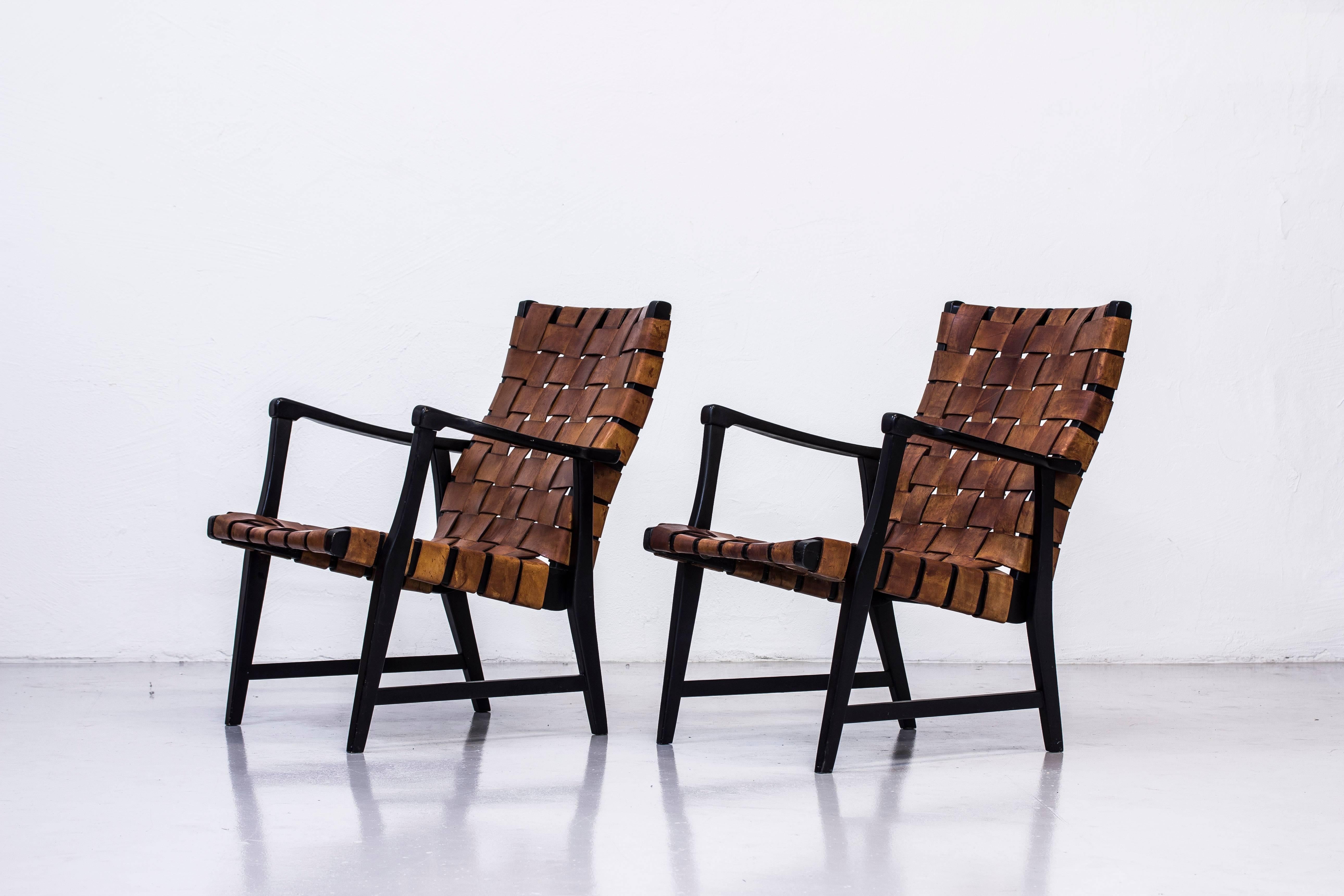 Rare pair of easy chairs designed by Elias Svedberg. Produced in Sweden by Nordiska Kompaniet during the 1940s. Black lacquered beech frame with thick cognac leather straps with great patina. Very good condition with age related wear and light