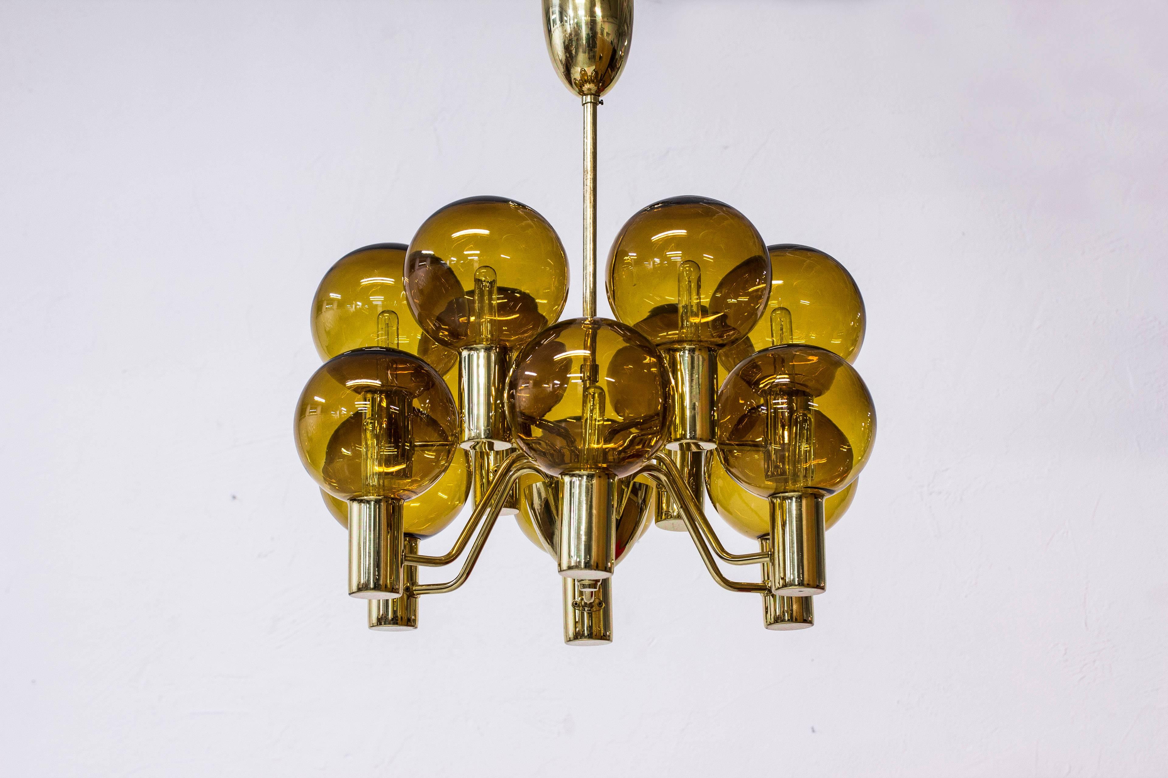 Chandelier model T372/12 designed by Hans Agne Jakobsson. Produced in Sweden by his own company in Markaryd during the 1960s. Made from solid polished brass with 12 arms and 12 handblown amber colored glass shades. Excellent vintage condition with