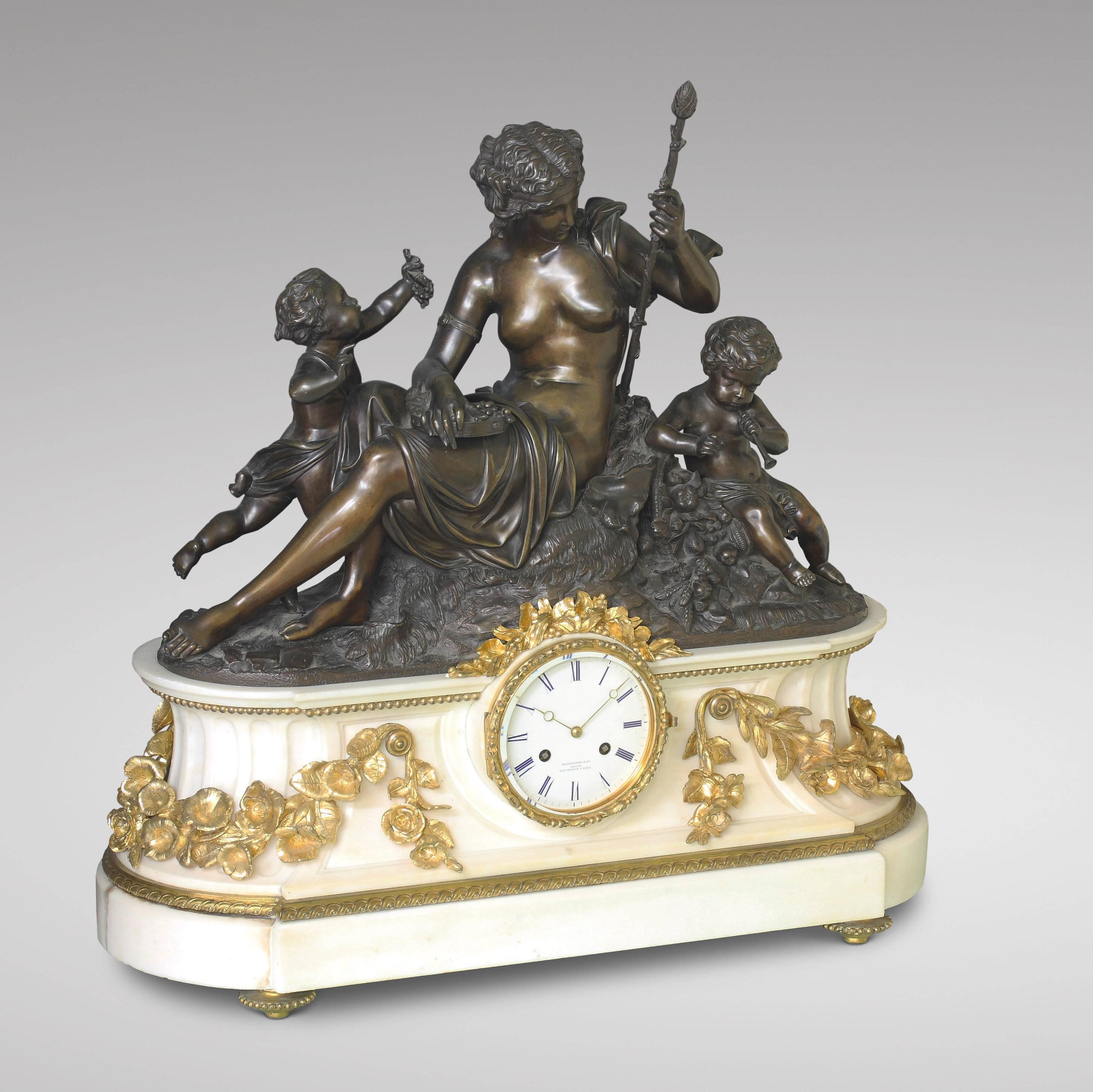 Large patinated bronze group with a sitting bacchante and two putti, one offering a bunch of grapes and the other playing a flute. Imposing white marble base decorated with gilded flower garlands on four ormolu toupee feet, with an enamel dial