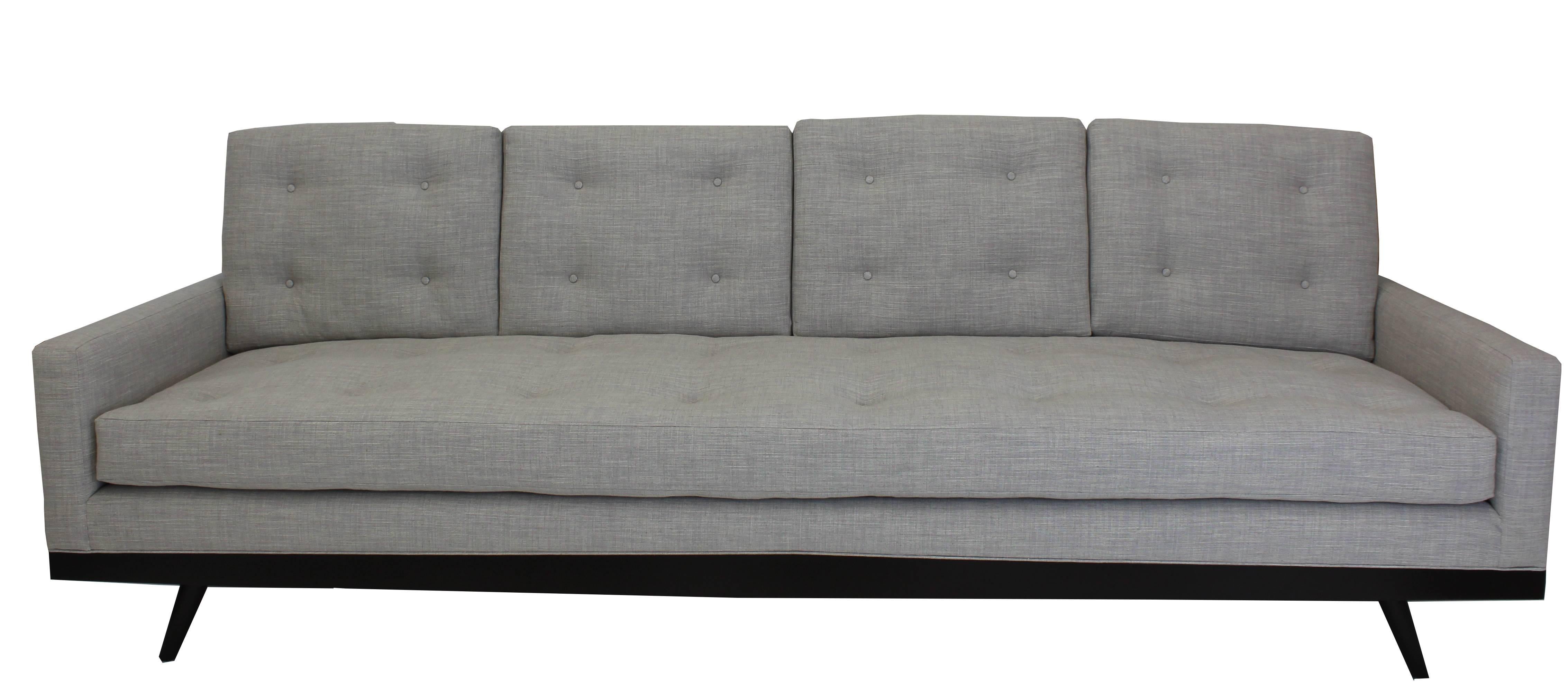 Dieses moderne Sofa ist ein ausgeprägtes Wohnzimmersofa, das sich an der Schnittstelle zwischen Mid-Century und heute befindet, mit klaren Linien und maßgeschneiderten Kissen, die fachmännisch von Hand getuftet sind. Das Möbelstück hat einen Sockel