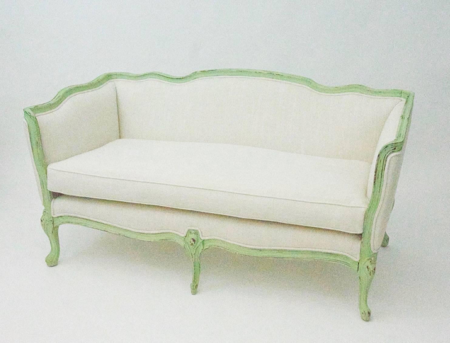 Vintage Country French style Settee upholstered in linen blend, featuring a bench cushion. Painted wood frame has a distressed, aged patina look.