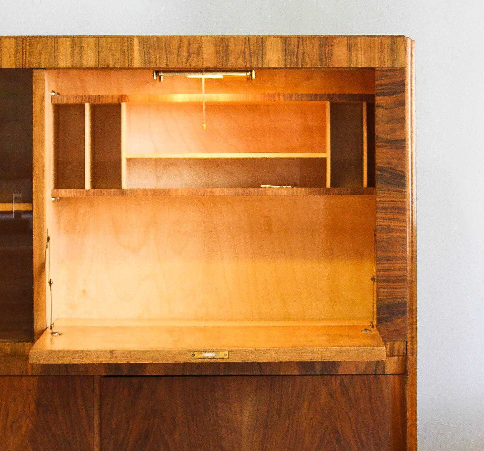 Beautiful “Art Deco” secretairy in burlwood.

The cabinet is in perfect condition.

The secretairy has build-in light.

Next to the secretairy is a cabinet with glas sliding doors. The corner is made of curved glass. Nice detail!

Below the