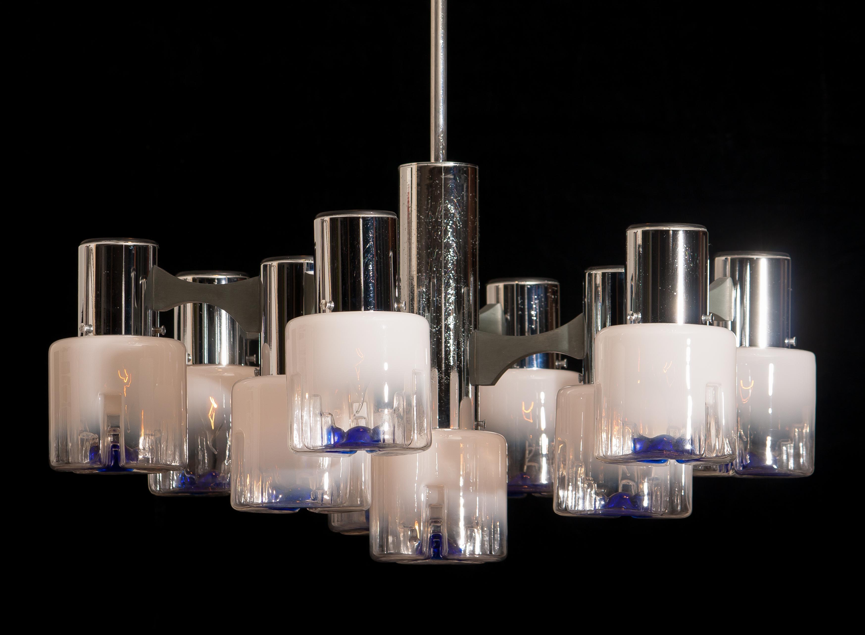 Mazzega chandelier in the fabulous design of the 1970 and filled with Murano crystal overflowing shades.
Chromed steel frame. Ten crystal shades of Murano Mazzega. The shades are overflowing from white to transparent and in the bottom a blue