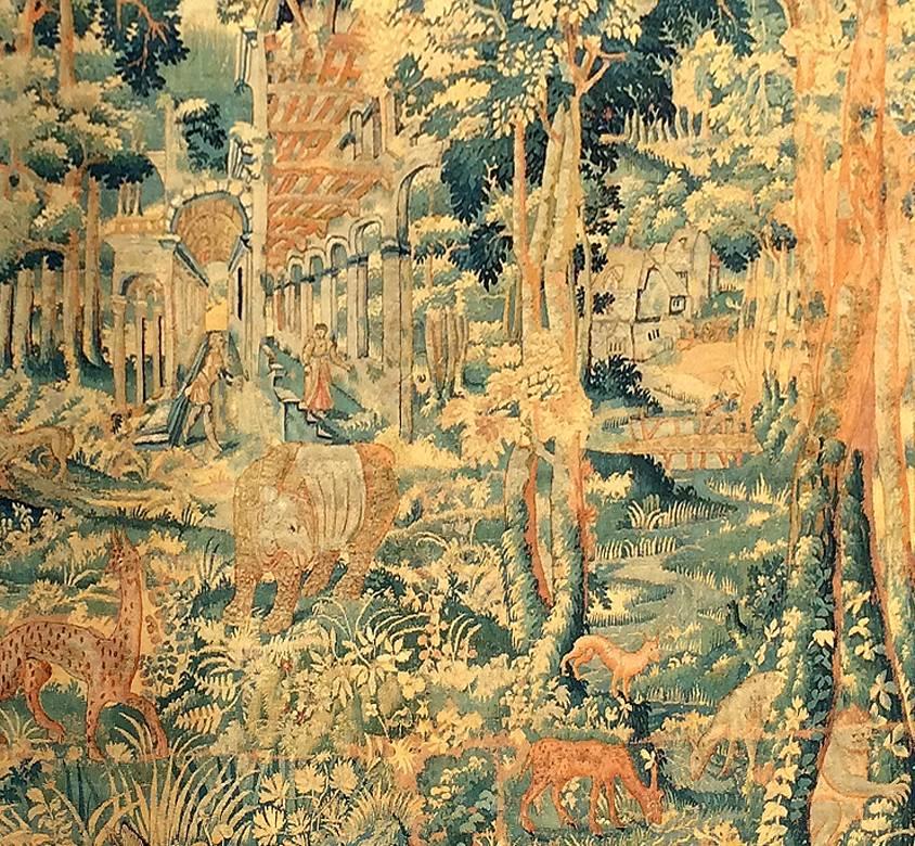 Flemish, mid-late 17th century. Detailed handwoven tapestry textile panel with a complex composition depicting a village in the background flanked by a forest. Animals and people can be found throughout the piece. Flowers and more foliage make the