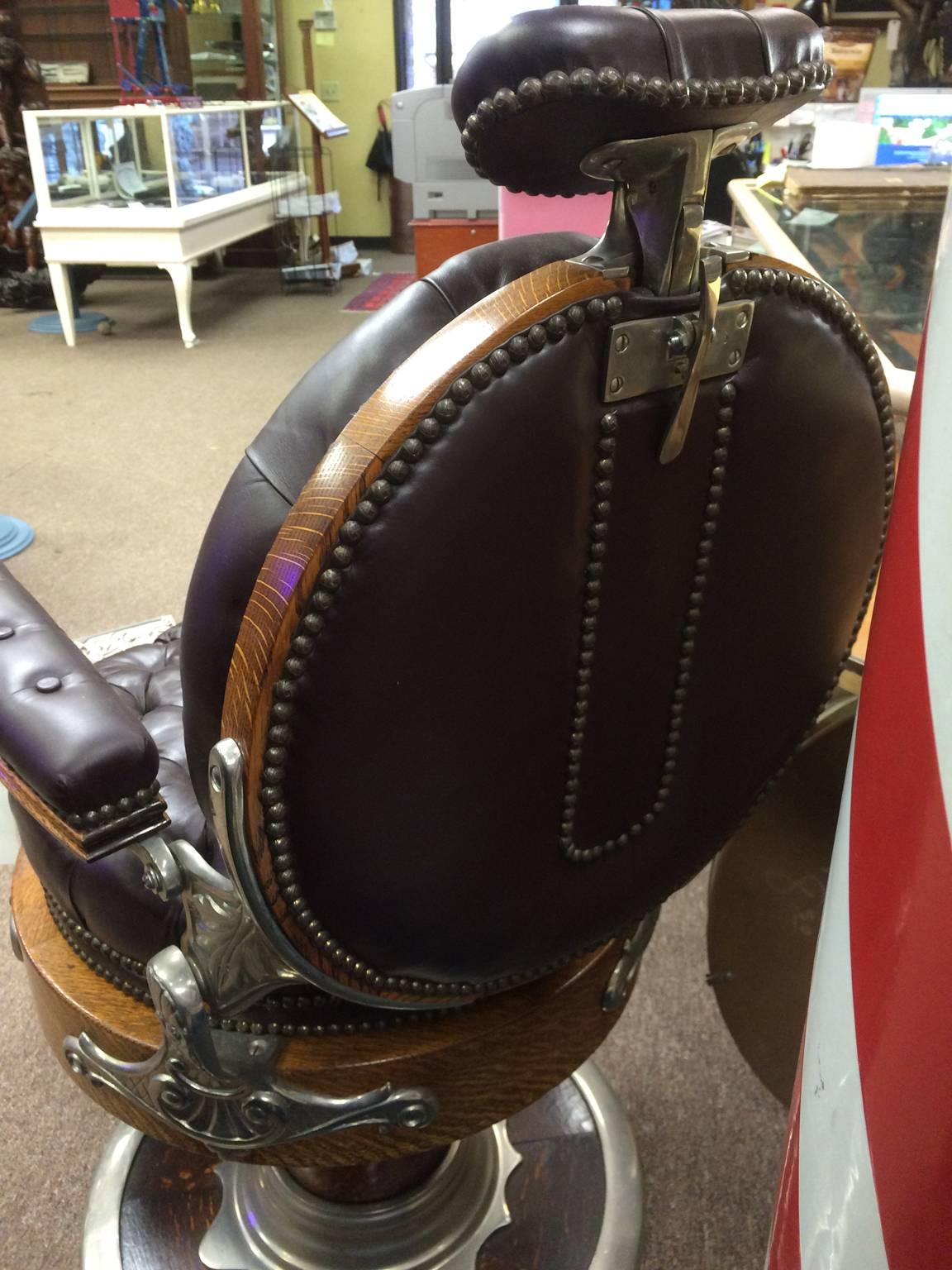 Fully restored round oak seat Kochs barber chair upholstered in fine tufted glove leather by Sam Robbins. The Theo. A. Kochs Company, established in Chicago, circa 1800s, was one of the first companies to be in the barber supply business. Their