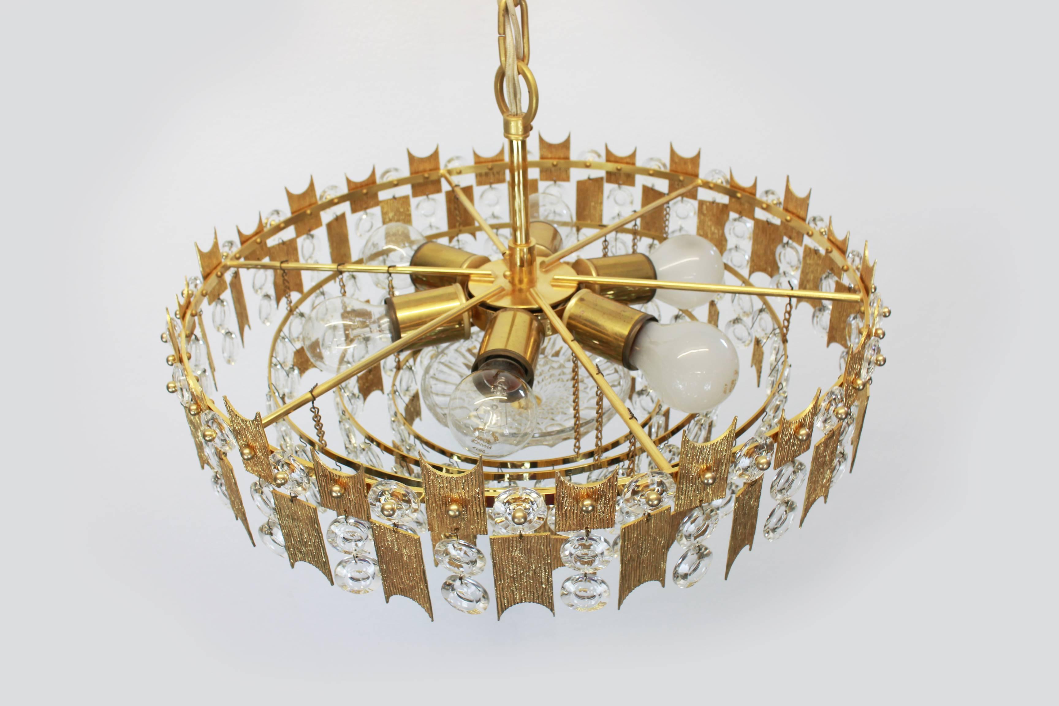 A stunning chandelier by Palwa (Palme and Walter), Germany, manufactured in 1960s. It’s composed of jewel-like glass pieces and brass plates with a Brutalist relief.

Sockets: It needs six x E27 standard bulbs to illuminate.
Perfect