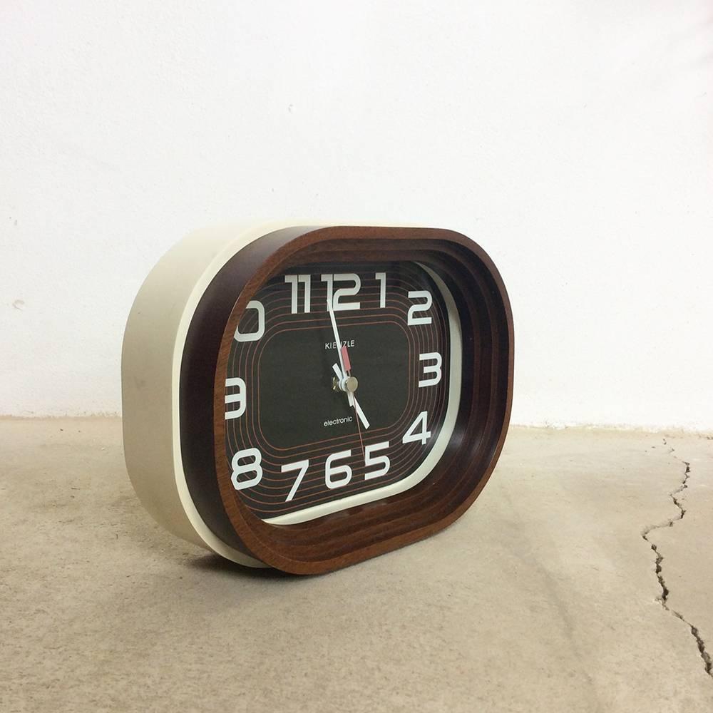 Wall and table clock.

Producer Kienzle, Germany,

1970s.

This wooden clock was manufactured by Kienzle Electronic in Germany in the 1970s. It is made from lacquered wood with the foot ring made from solid teak. The clockwork is a renewed
