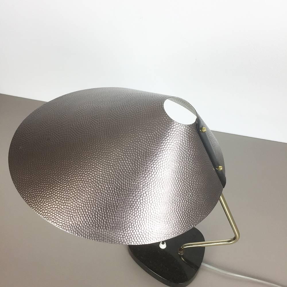 Table light. 

Origin: Germany,

1950s.

Original 1960s table light made in Germany. this wonderful modernist 1960s table light comes with a huge japanse hut formed metal shade in leather perforation optic and a wonderful granite stone