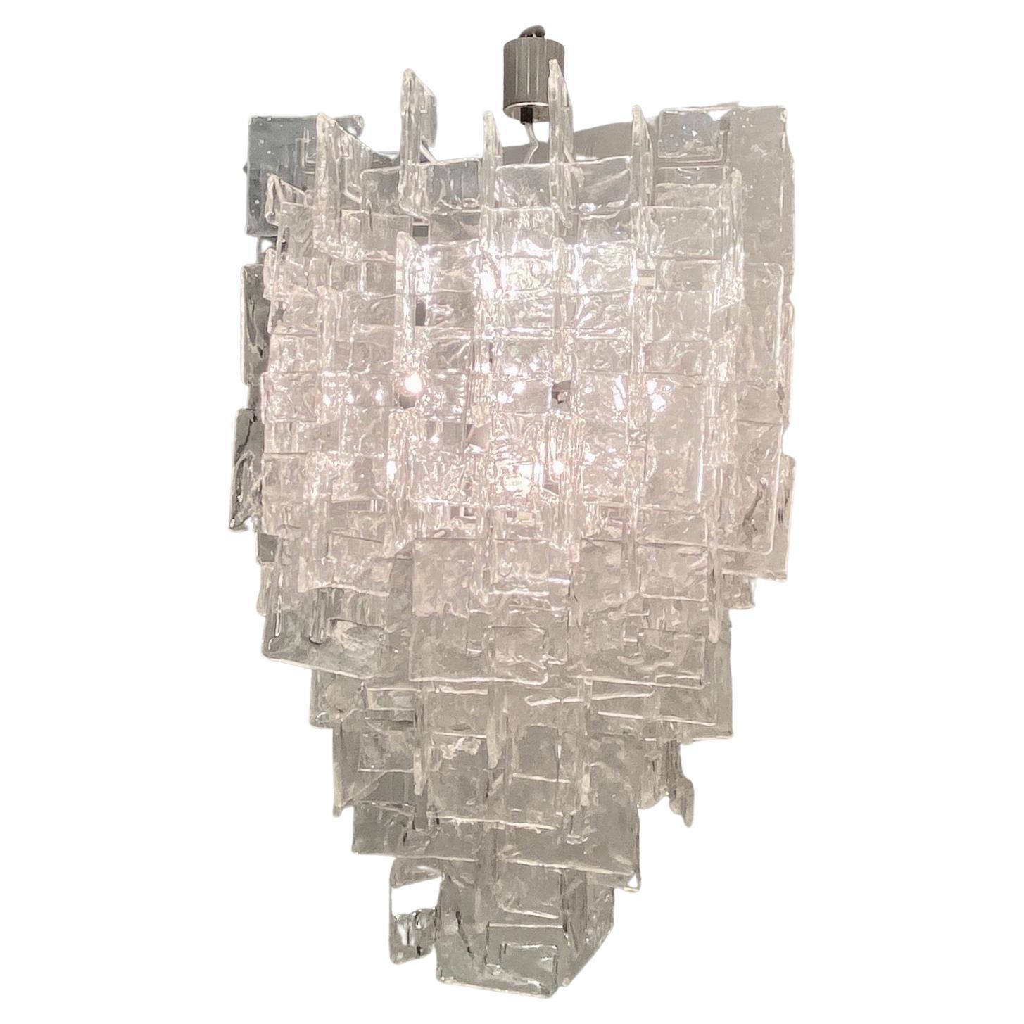 Il s'agit d'un lustre Murano classique à 12 ampoules des années 1960 avec environ 180 éléments en verre transparent Mazzega Murano en forme de C, tous originaux des années 60/70 (avec les éléments en verre d'origine de plus petite taille). La forme