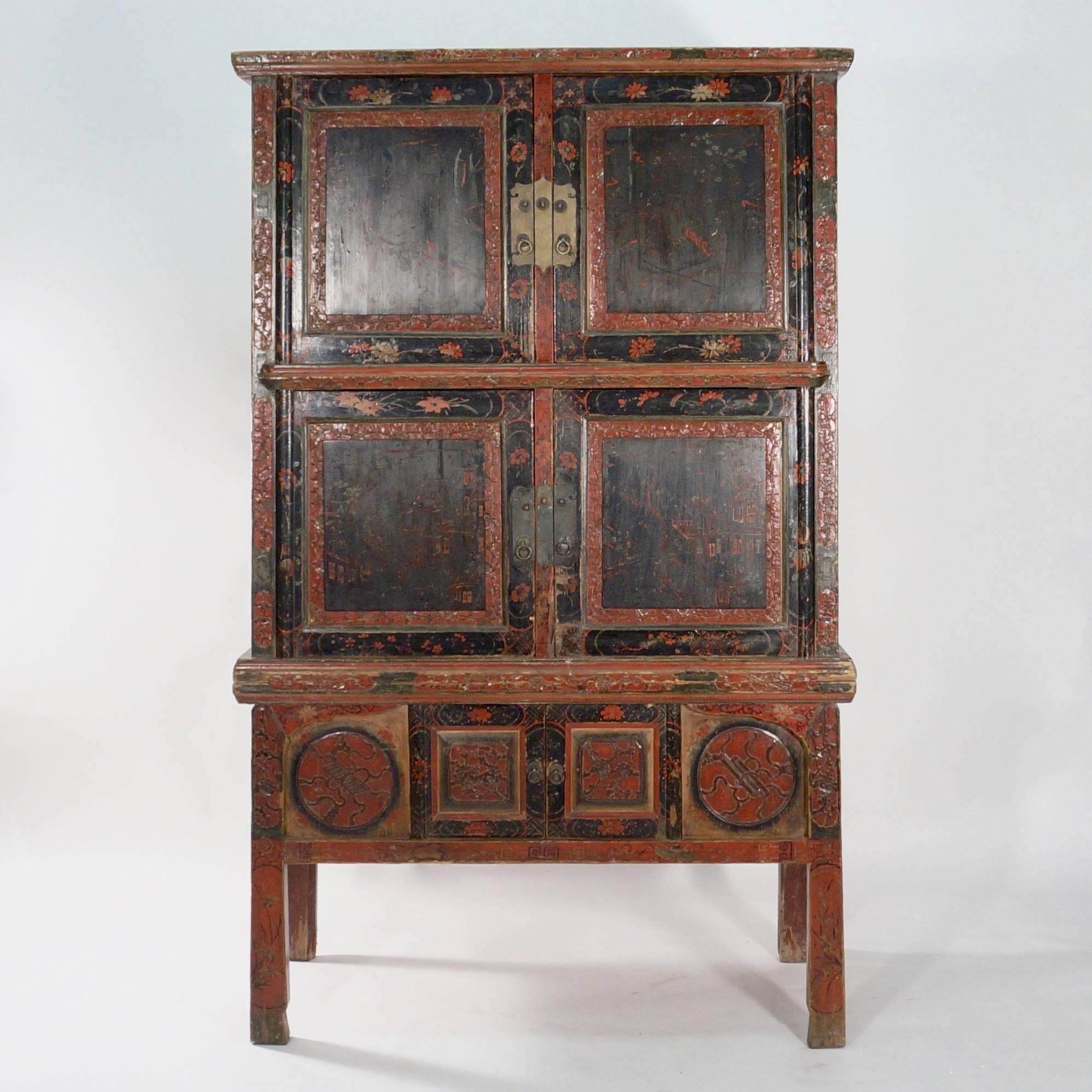 With four-panelled cupboard doors decorated with chinoiserie scenes in black and red lacquer with carved fillets and floral borders. The lower section with four legs supporting a cupboard to the apron flanked by roundels.

China, circa 1900.