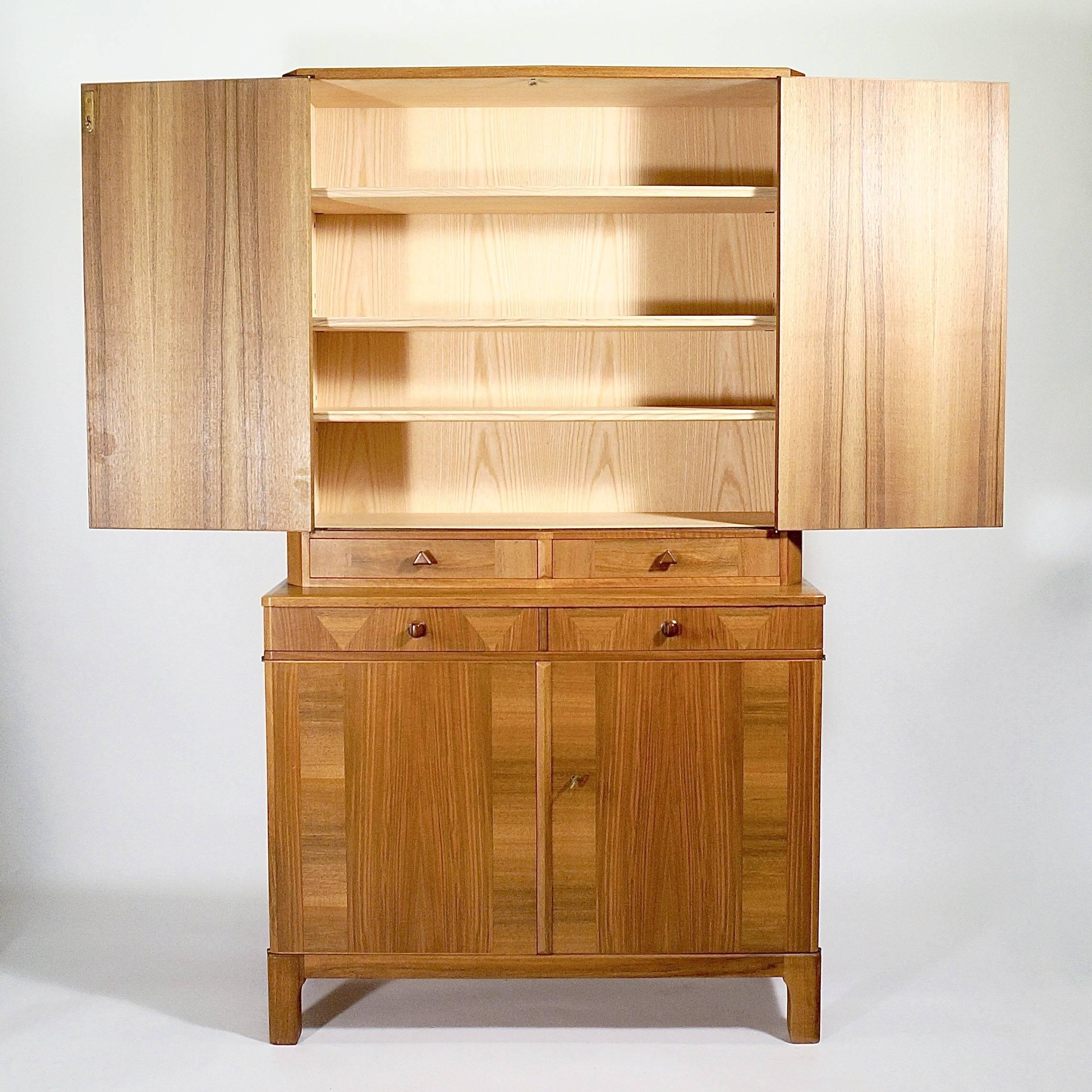 A walnut parquetry veneered cabinet in two parts. The upper section with two slightly canted doors above two conforming drawers, the lower section with two drawers above two doors. Both sections with shelved interiors.

Designed for Afors