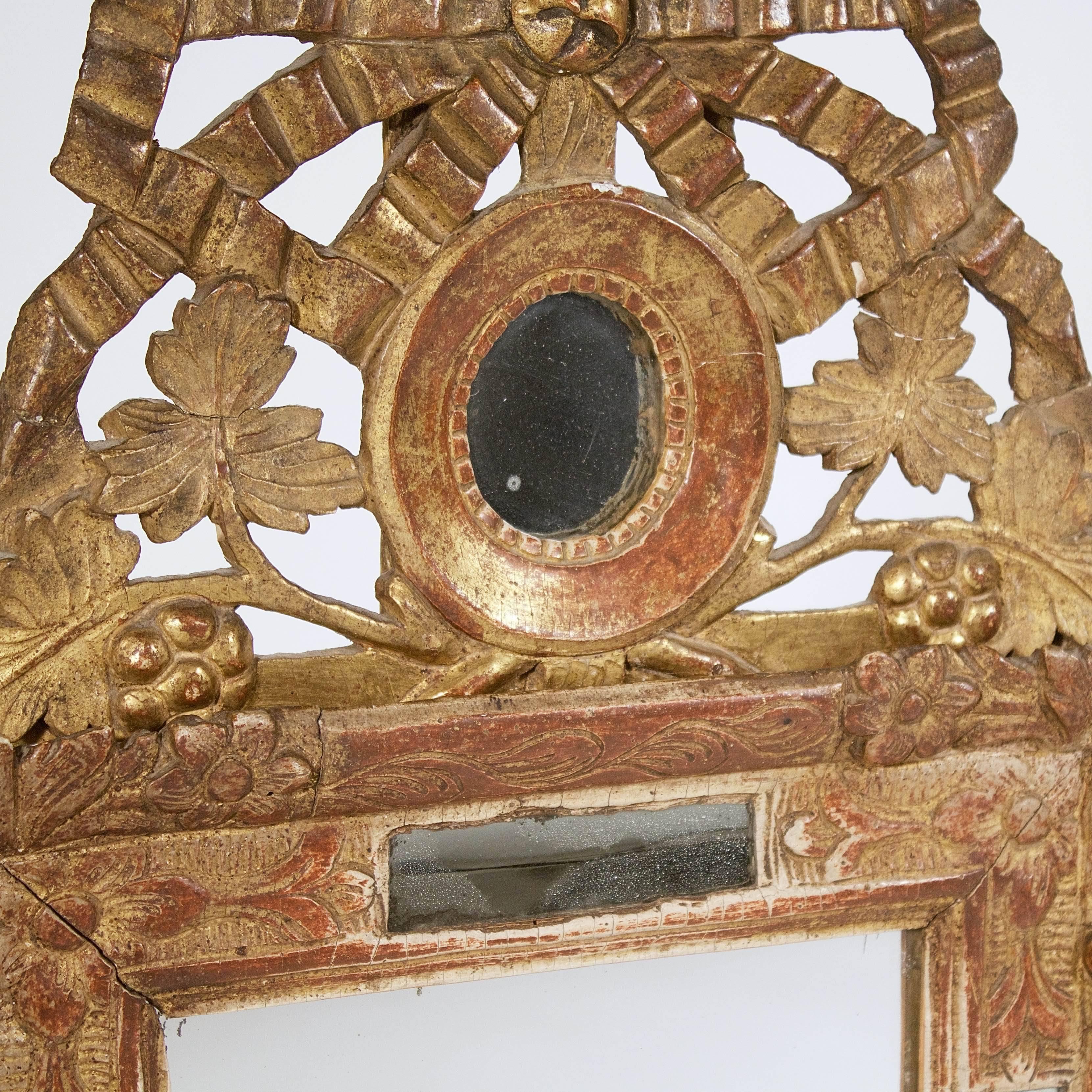 The rectangular mirror with a border glass and carved floral decoration supporting a pierced ribbon crest and a central oval mirror.

France, circa 1780s.