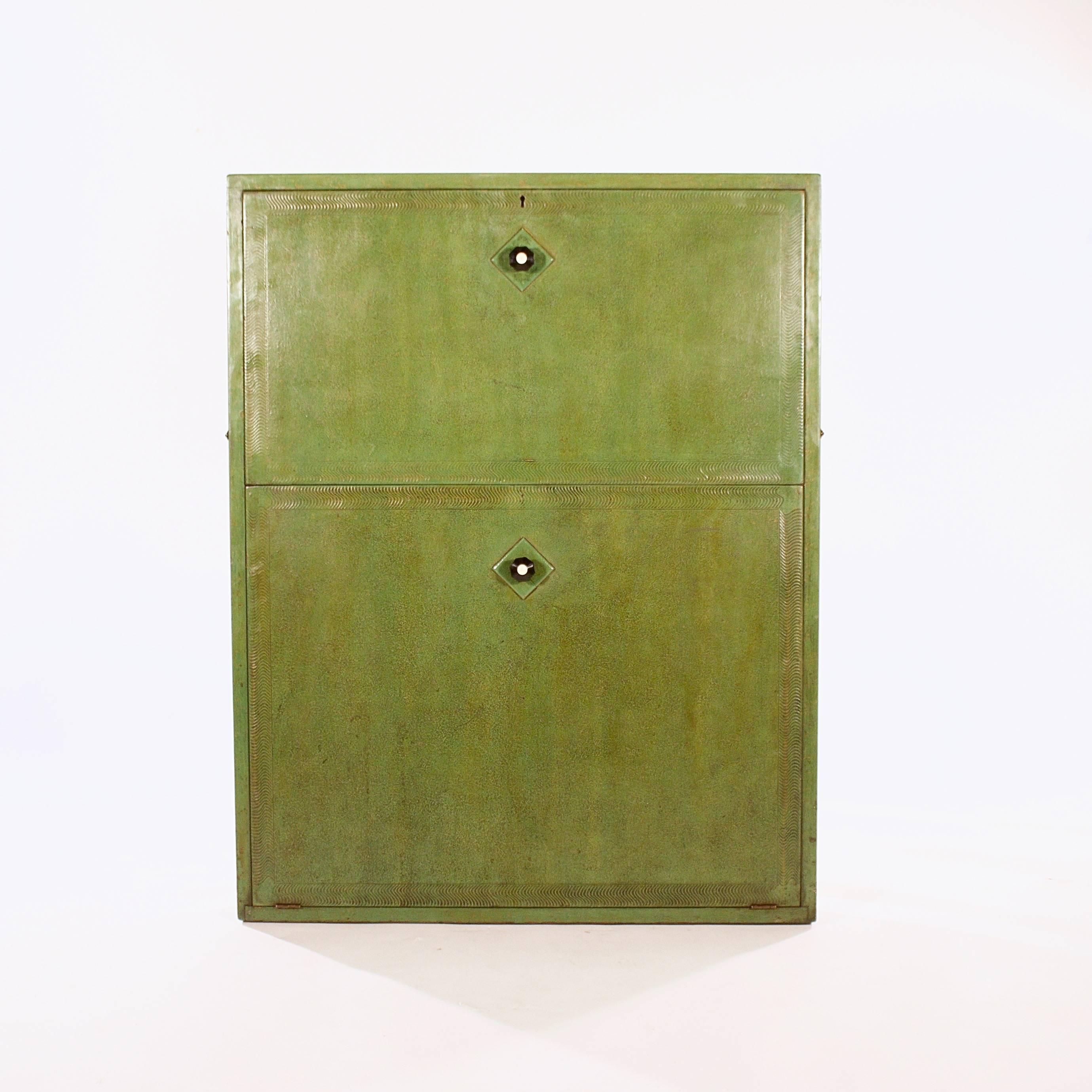 The front decorated with green stippled paint and pressed ripple borders enclosing a fitted interior to the fold-down top section and storage compartment to the bottom. Both the top and bottom sections with the original Bakelite handles.

With the