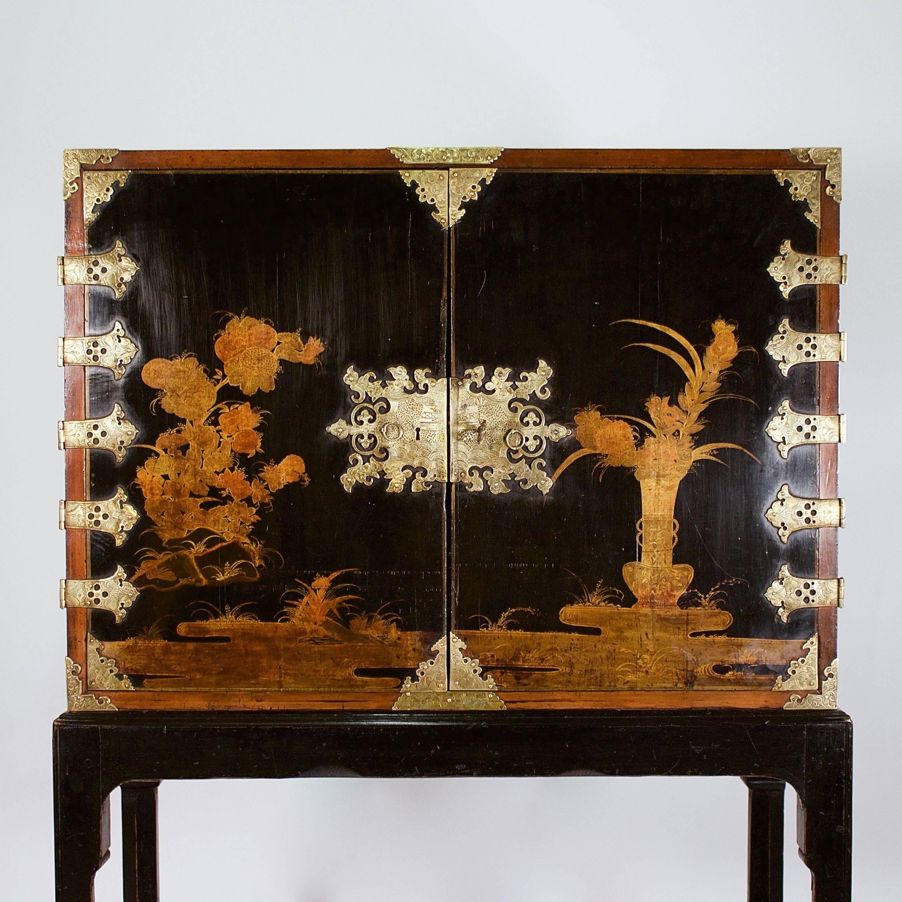 The two doors with floral lacquer decoration on a black lacquer ground with fine chased brass hinges and escutcheons enclosing a series of ten drawers of various sizes each decorated with village scenes and each drawer divided by nashiji lacquer