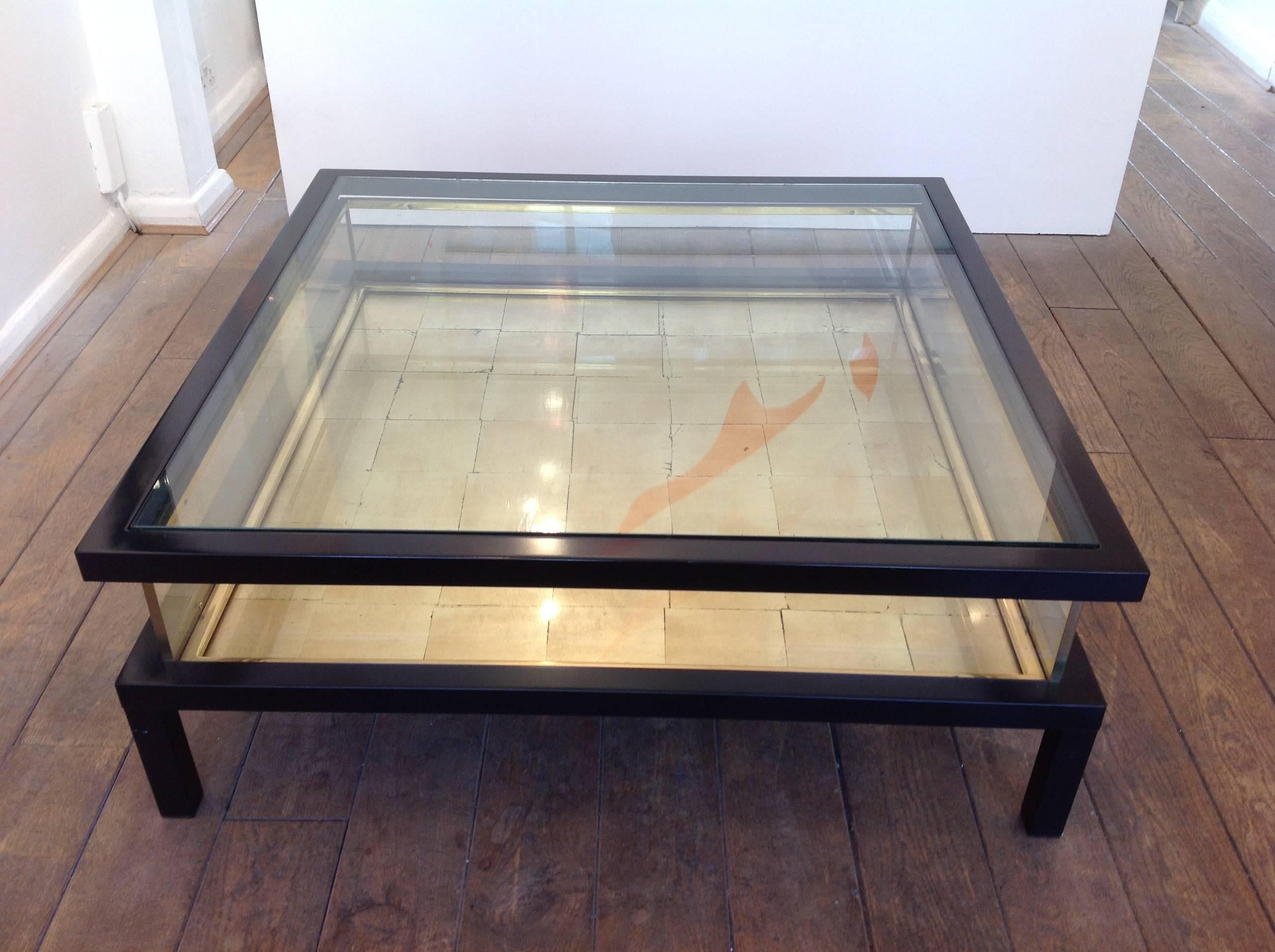 A unique version of the Maison Jansen sliding coffee table with black lacquer frame and brass trims. The top slides back on runners to reveal the inside, which has real gold leaf sheets laid under the glass base.