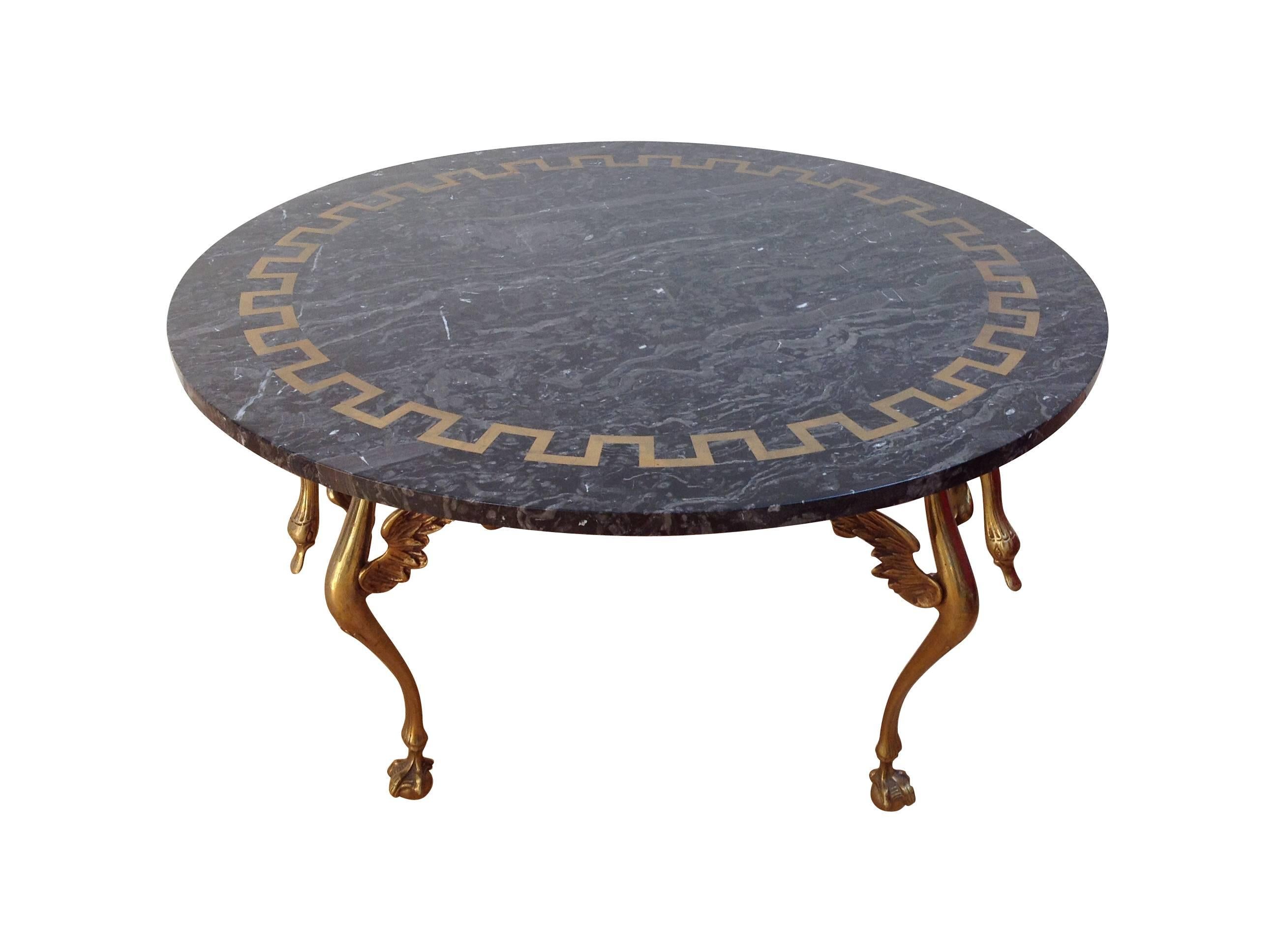 An Italian coffee/cocktail table with four legged brass base, each leg with winged swan neck on a ball and claw foot. The circular top of Belgian fossil marble with greek style brass inlay around the edge.