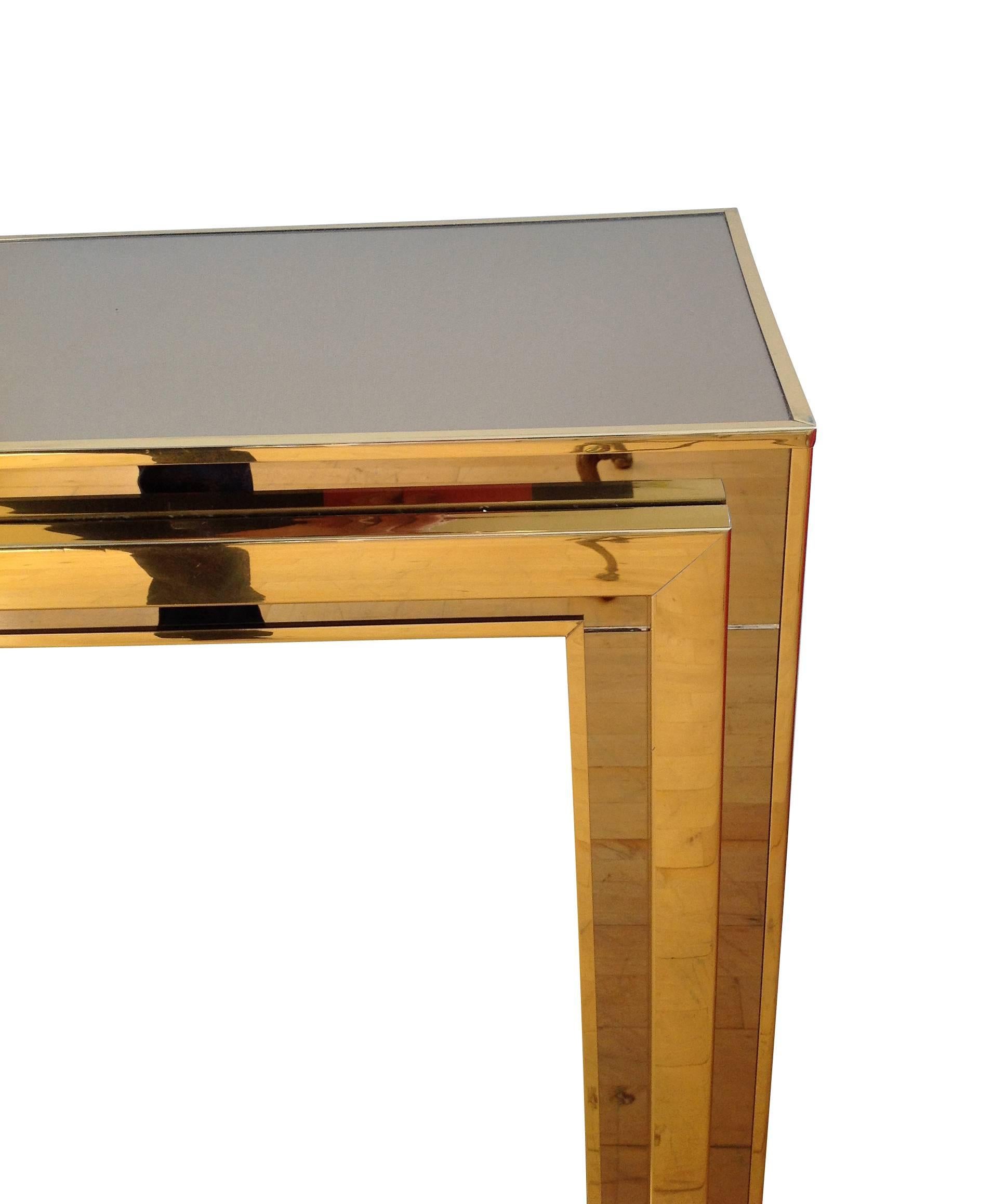 A smoked mirror and brass console, with mirrored top and legs, framed with a brass finish metal surround on all sides.