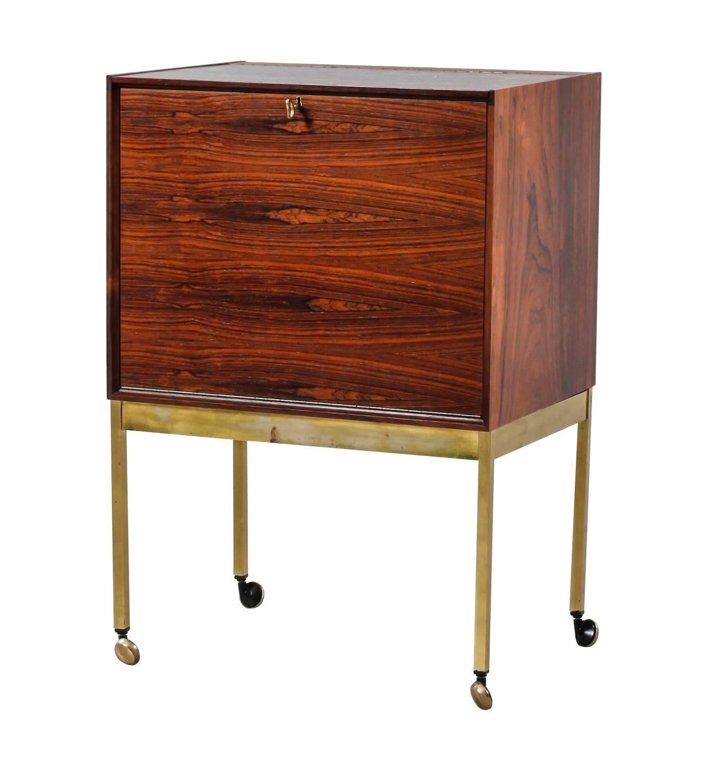 An Erik Buch Brazilian rosewood bar or drinks cabinet with hinged top and front, both with brass piano hinges and fittings with the original brass key and lock supported on brass legs and frame with original castors. The inside is mirrored with two